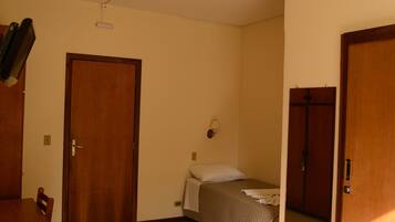 A room with a bed, a wooden door, a wall-mounted light, and a small table.