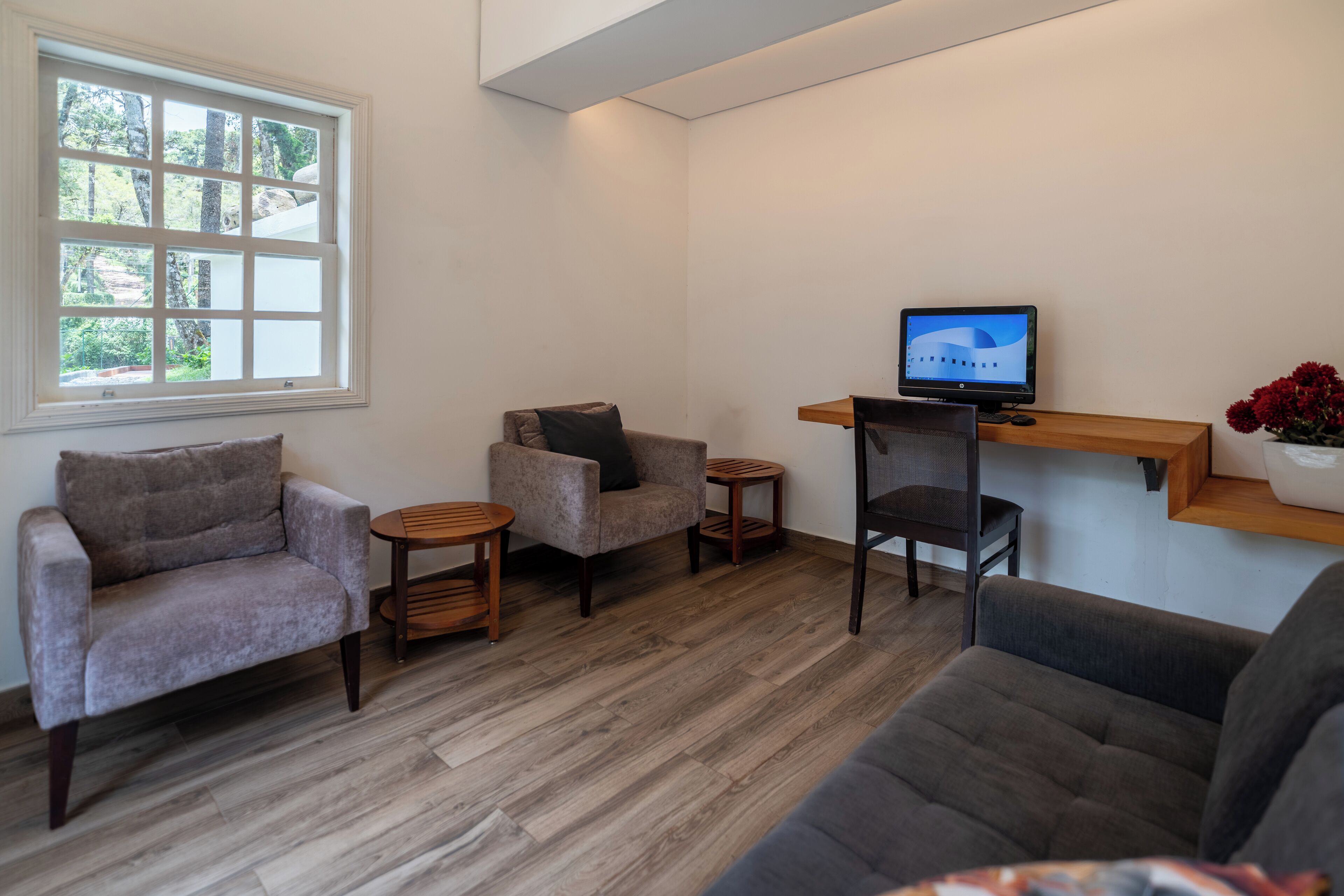 A modern living room with a grey sofa, a grey armchair, a small round table, and a television on a wooden stand.