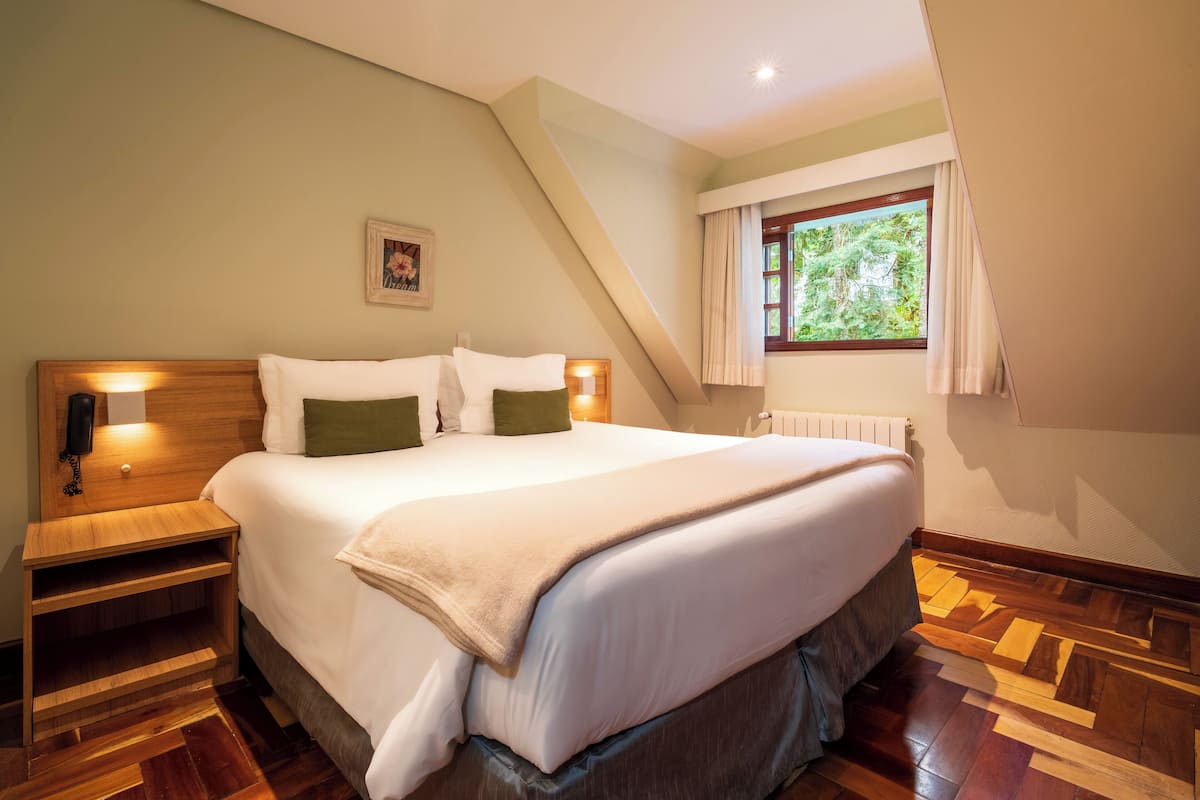 Un dormitorio ordenado con una cama grande, una mesita de noche, una ventana con cortinas y un radiador.