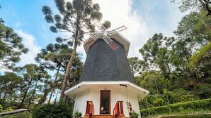 Eine traditionelle Windmühle mit weißem Unterbau und dunklem Dach, umgeben von üppiger Vegetation und hohen Bäumen.