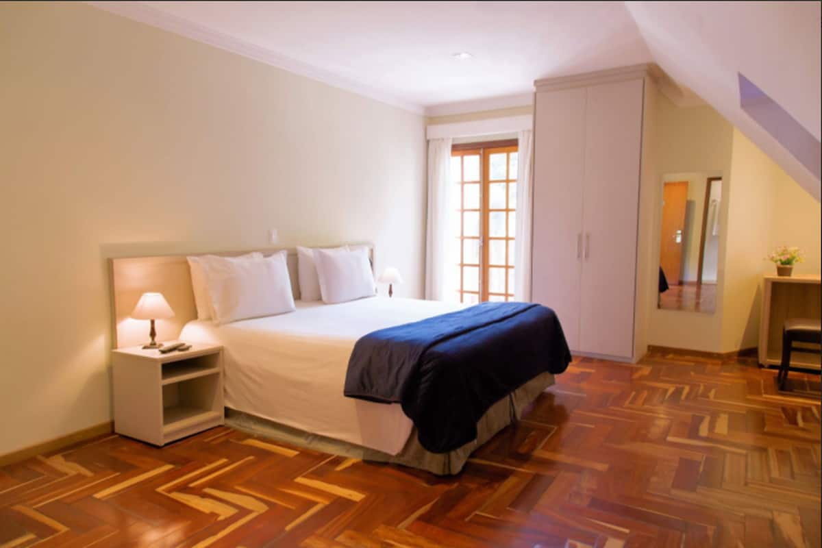 Un dormitorio con cama, mesita de noche y ventana con cortinas.