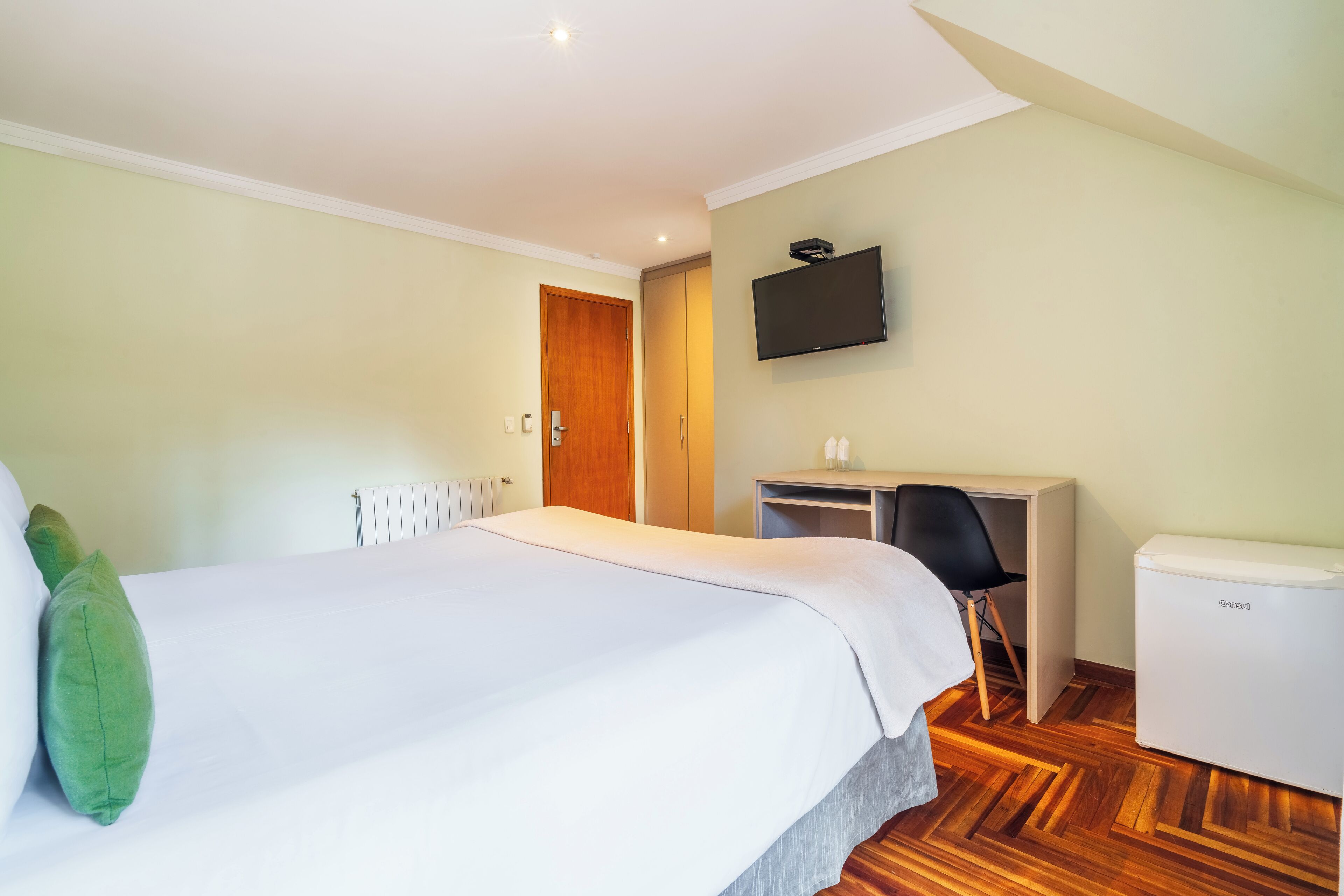 A hotel room with a bed, a desk, a chair, a television, and a radiator.