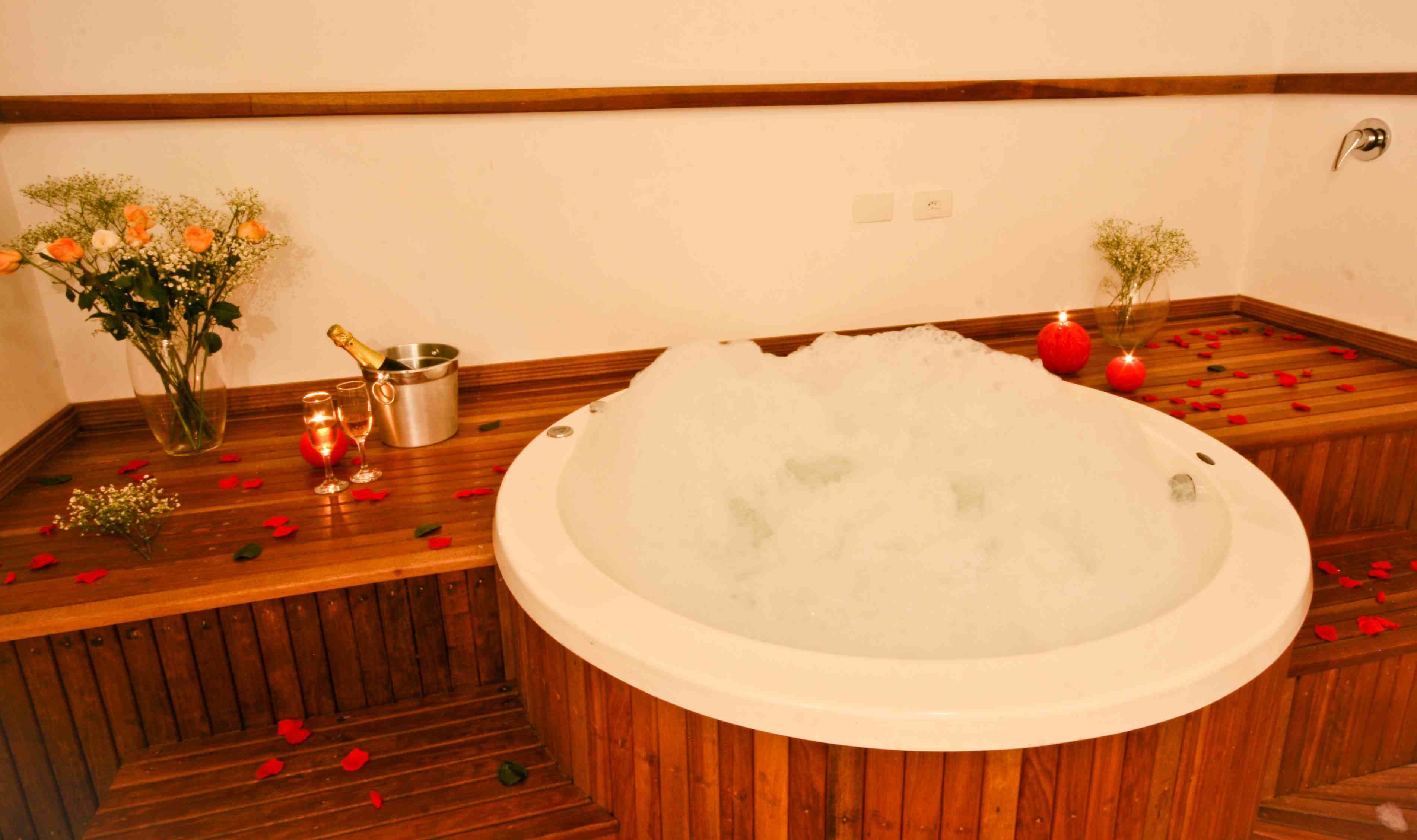 Une baignoire en bois remplie de glace, entourée de pétales de rose, avec une bouteille de champagne et un vase de fleurs.