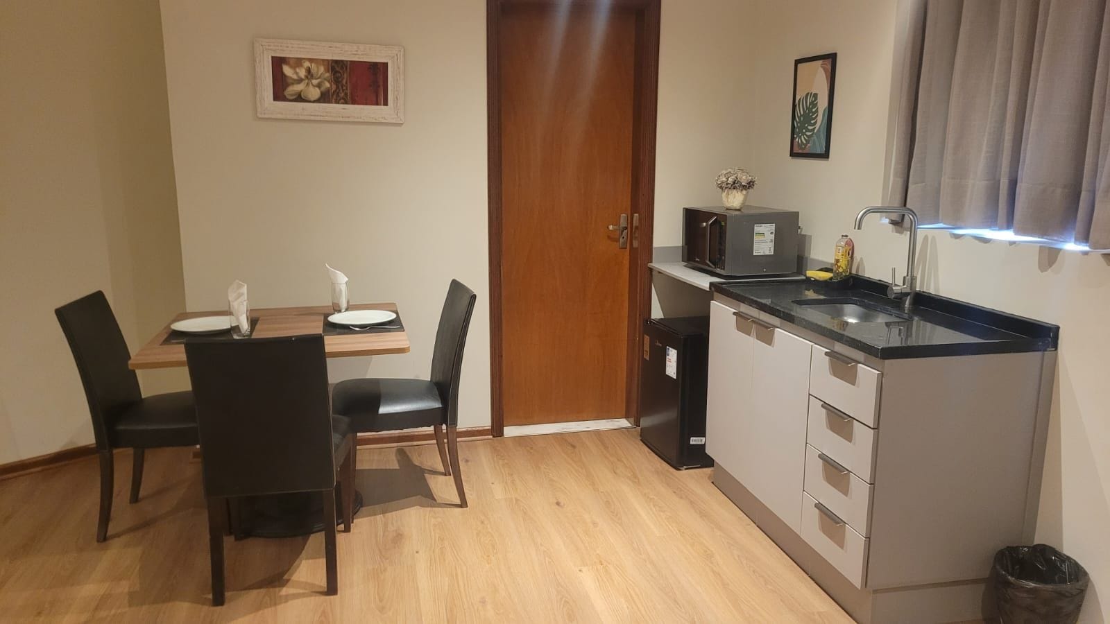 A compact kitchen with a dining table, chairs, a refrigerator, and a microwave.