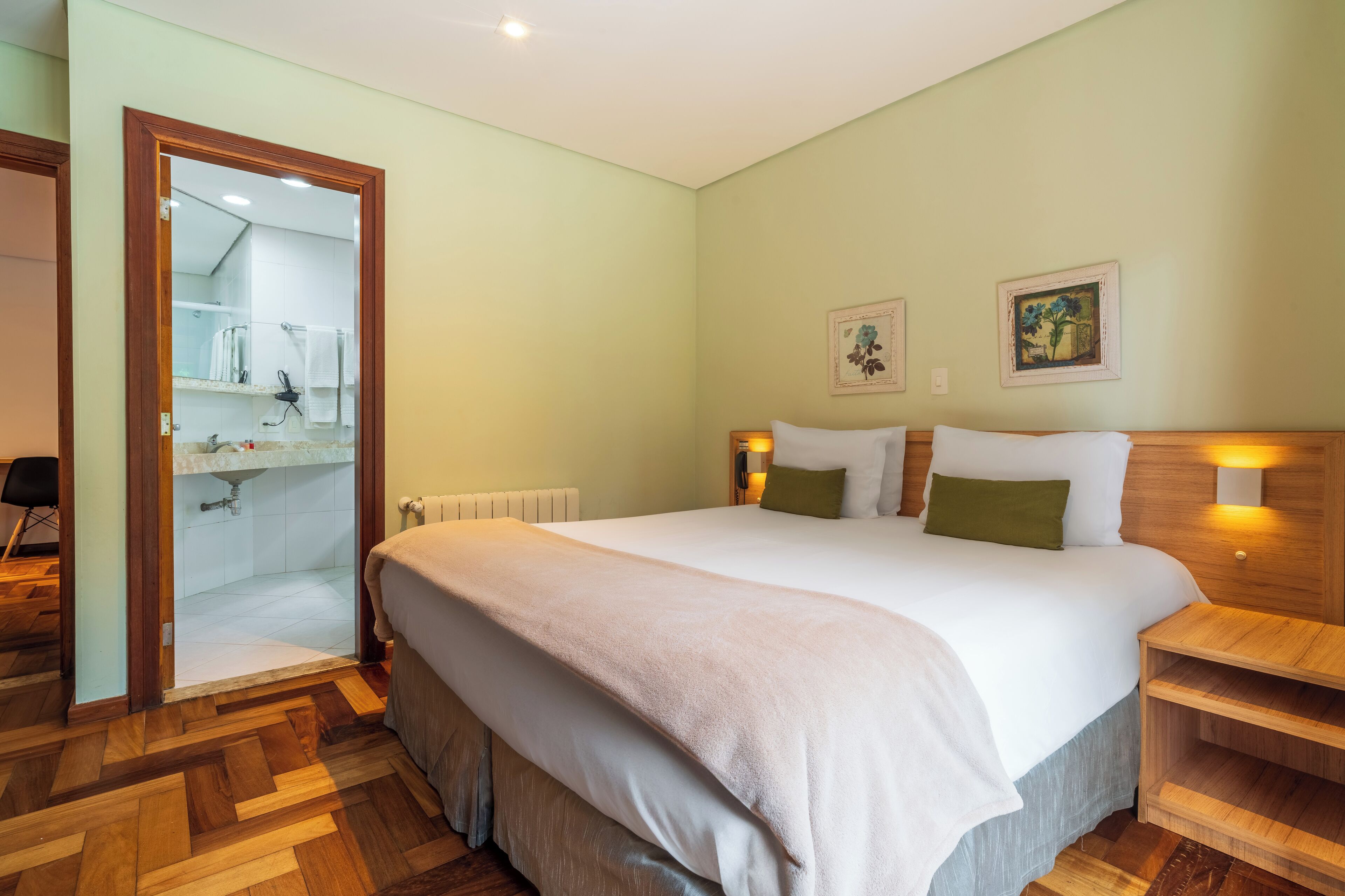 A hotel room with a large bed, wooden floor, a bathroom with a shower, and a wooden nightstand.