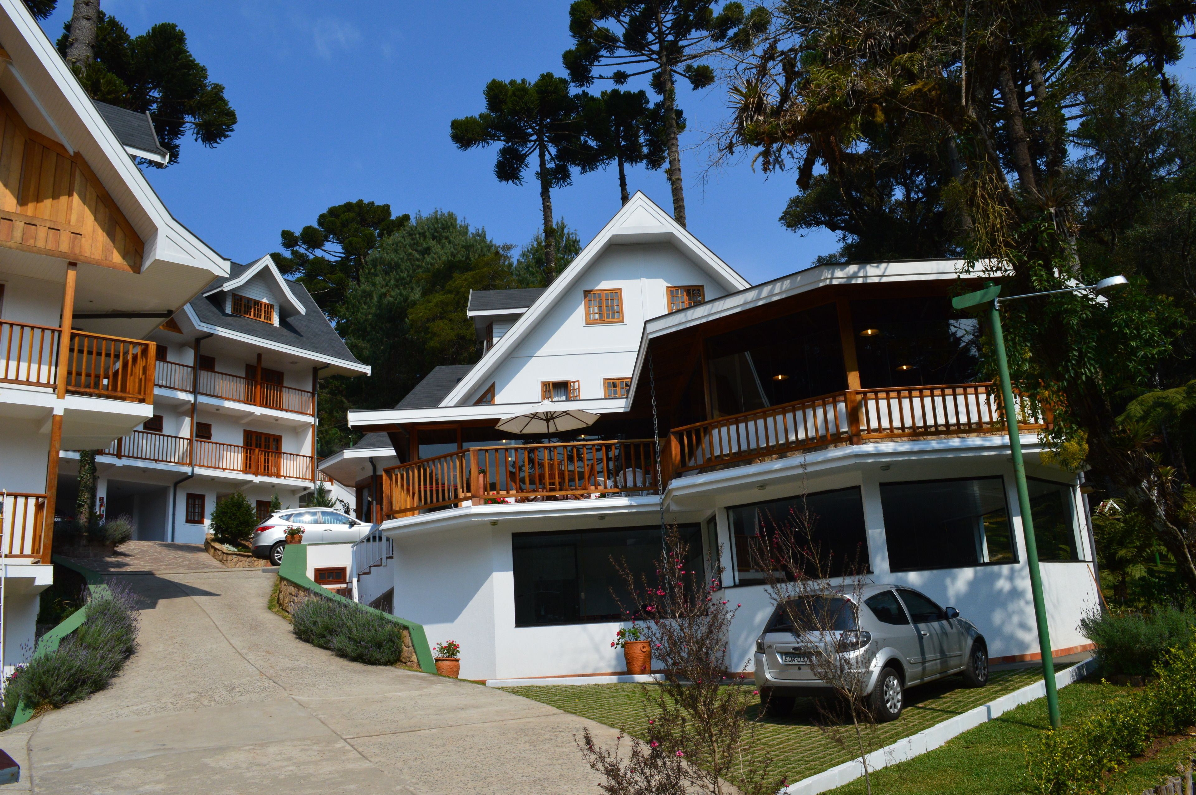 Un hotel de varios pisos con balcones, una zona de estar al aire libre cubierta y un coche estacionado en la entrada.