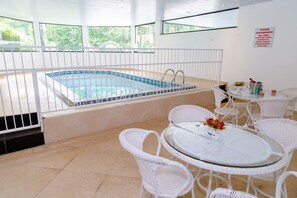 A pool area with a tiled pool, white wicker chairs, and a glass table with a flower vase. - Pousada Campos dos Holandeses (Campos do Jordão)