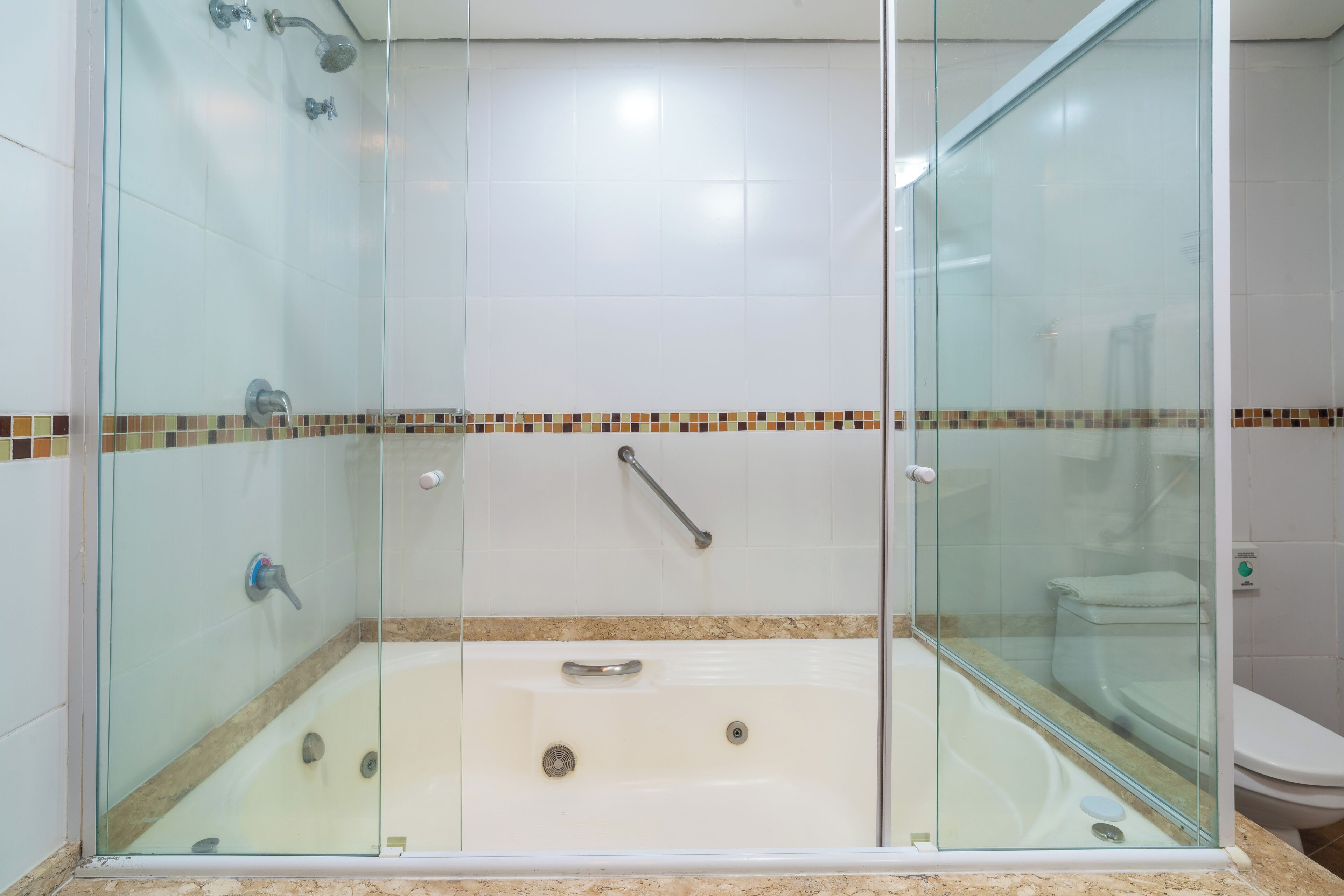 Zona de ducha con mampara de vidrio, una bañera, una puerta de cristal y piso de baldosas.