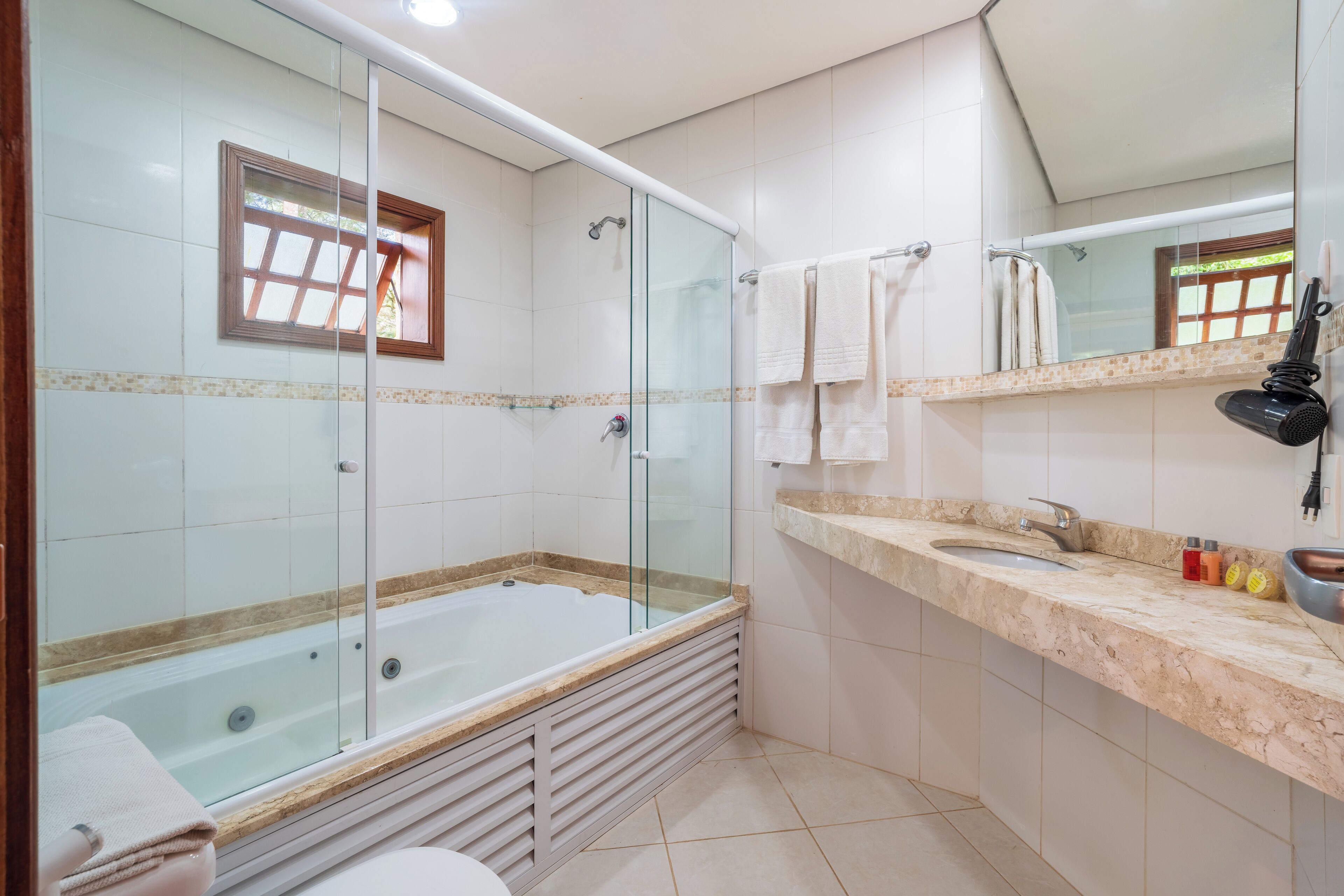 Un baño moderno con ducha de vidrio, bañera, lavamanos y tocador con artículos de aseo.