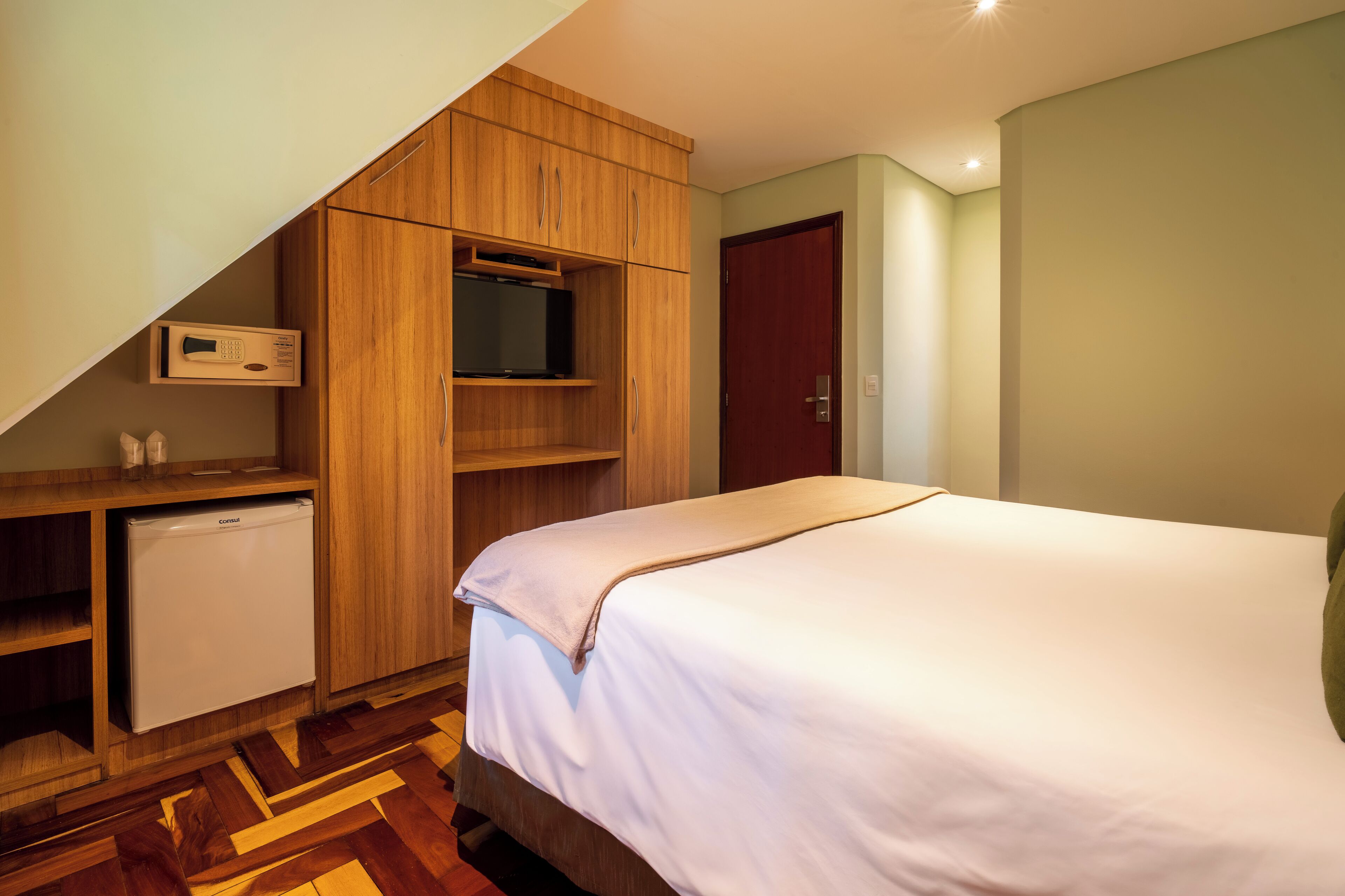 Un dormitorio con cama, televisor, refrigerador pequeño y armario.