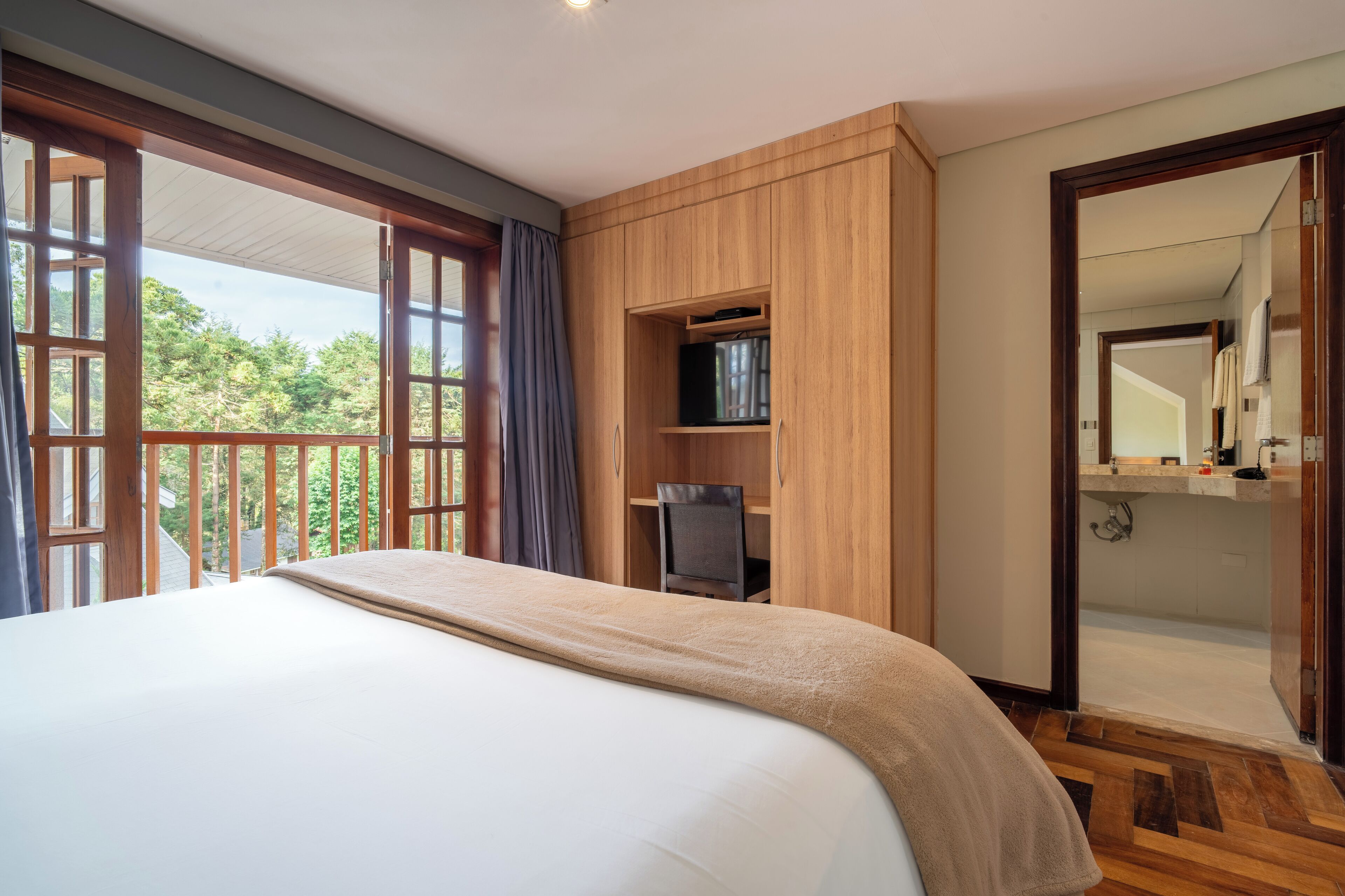 Un dormitorio con una cama grande, armario de madera, televisor y un baño visible a través de una puerta abierta.