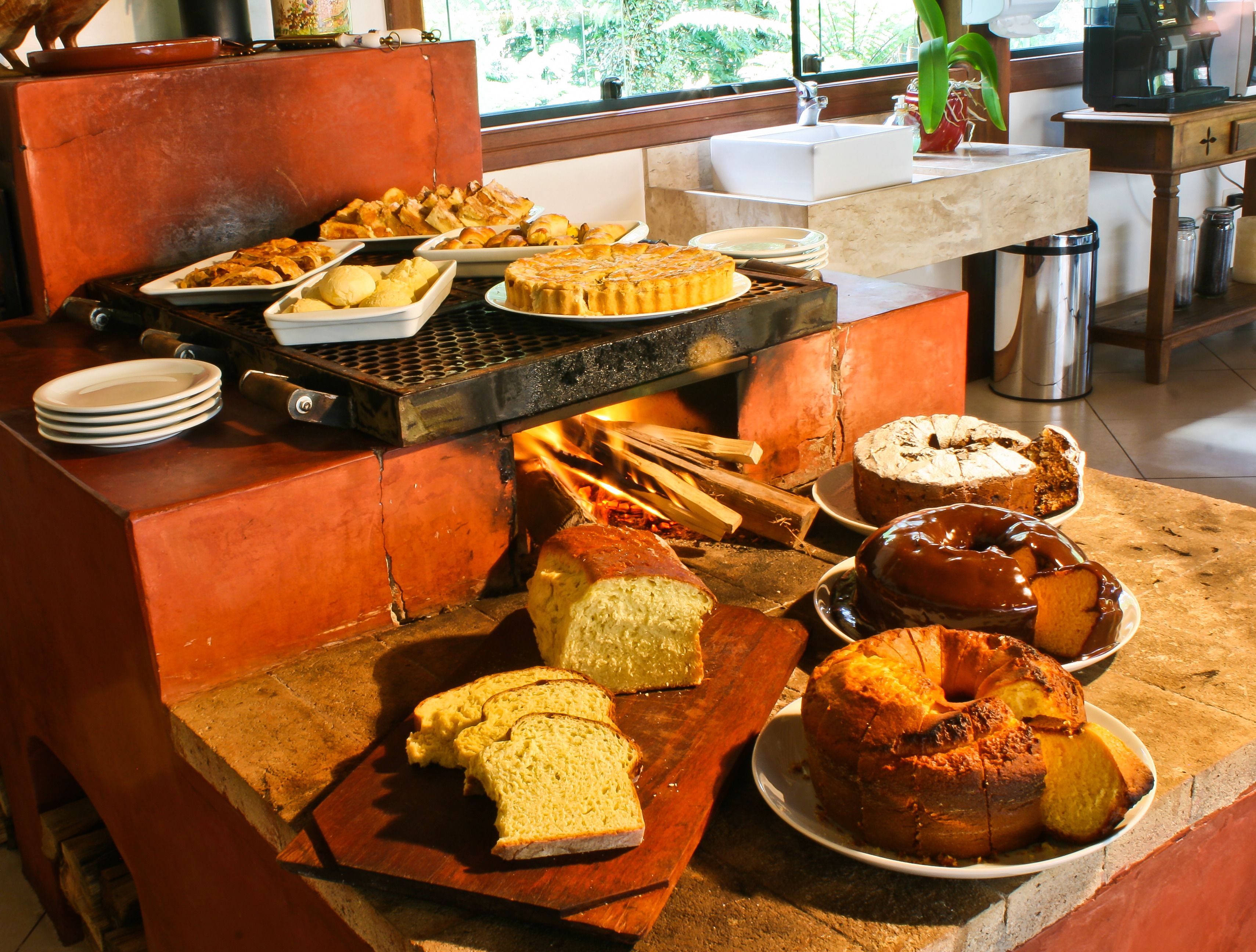A buffet with various baked goods, including bread, pies, and a cake, displayed on a wooden table in a kitchen area.