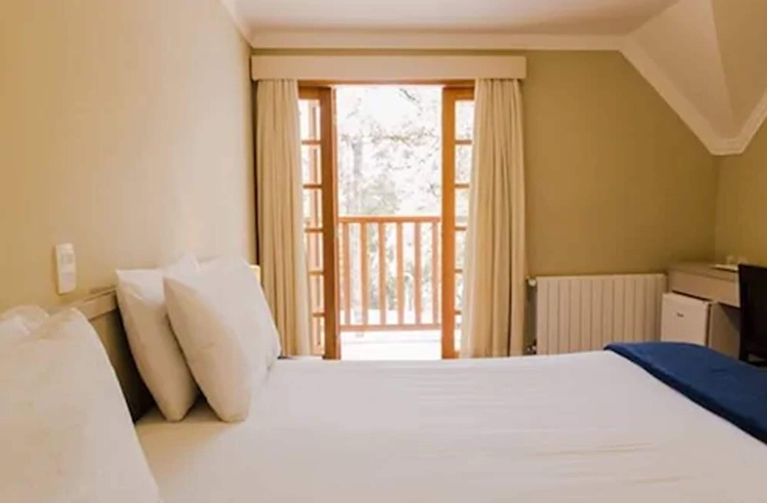 A bedroom with a bed, a desk, and a view of the outdoors.