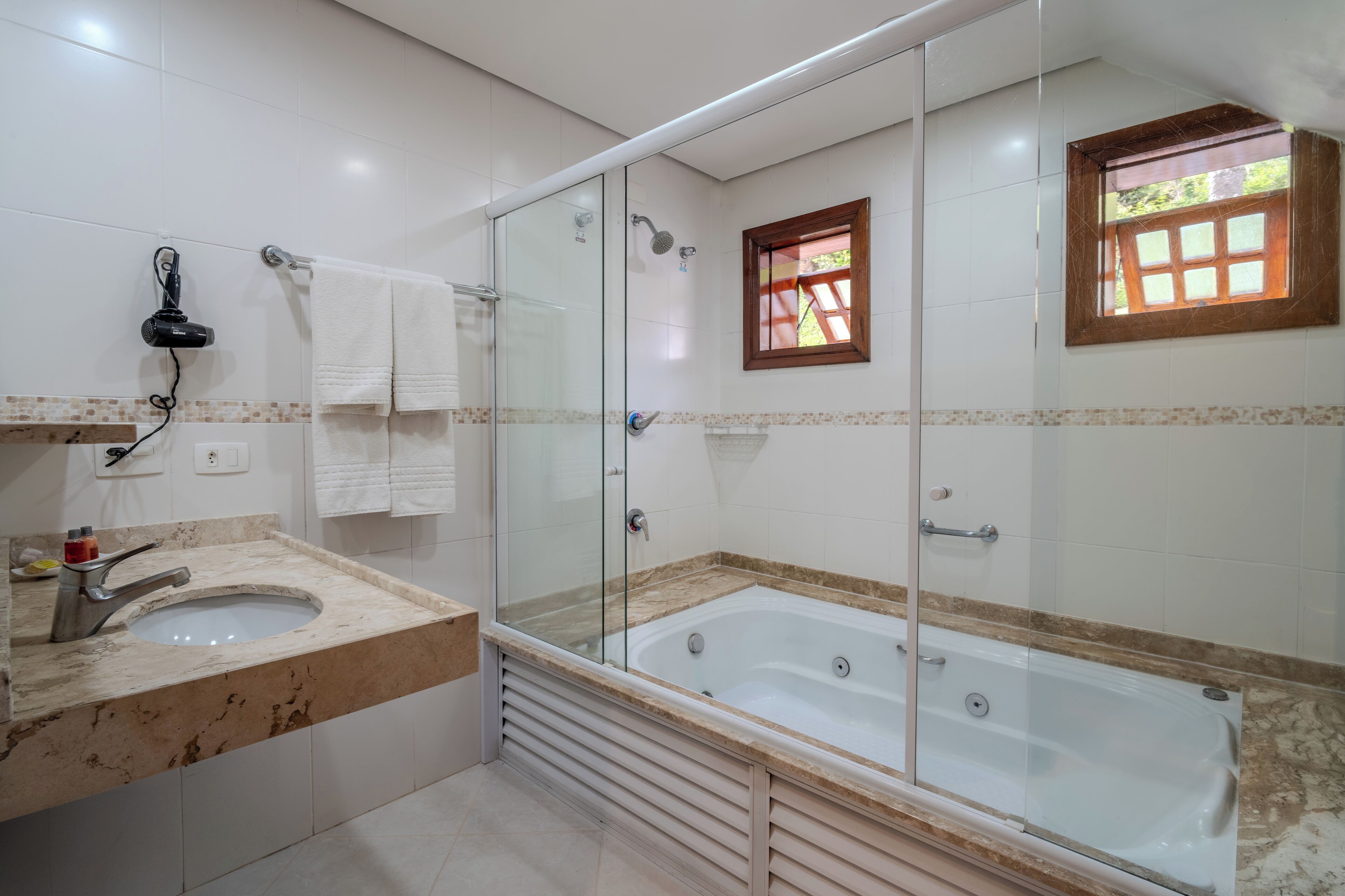 A modern bathroom with a glass-enclosed shower, a large bathtub, and a marble sink.