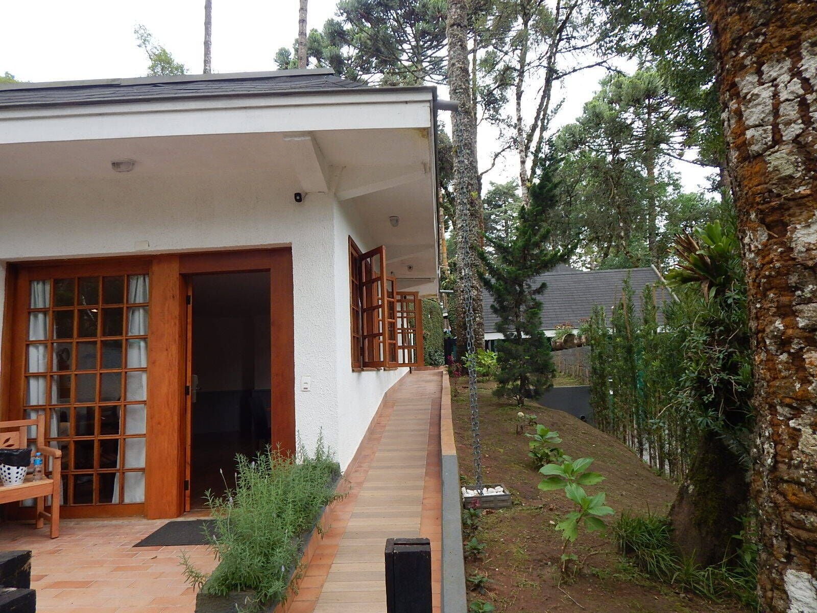 A house with a wooden deck, a covered porch, and a garden with various plants.