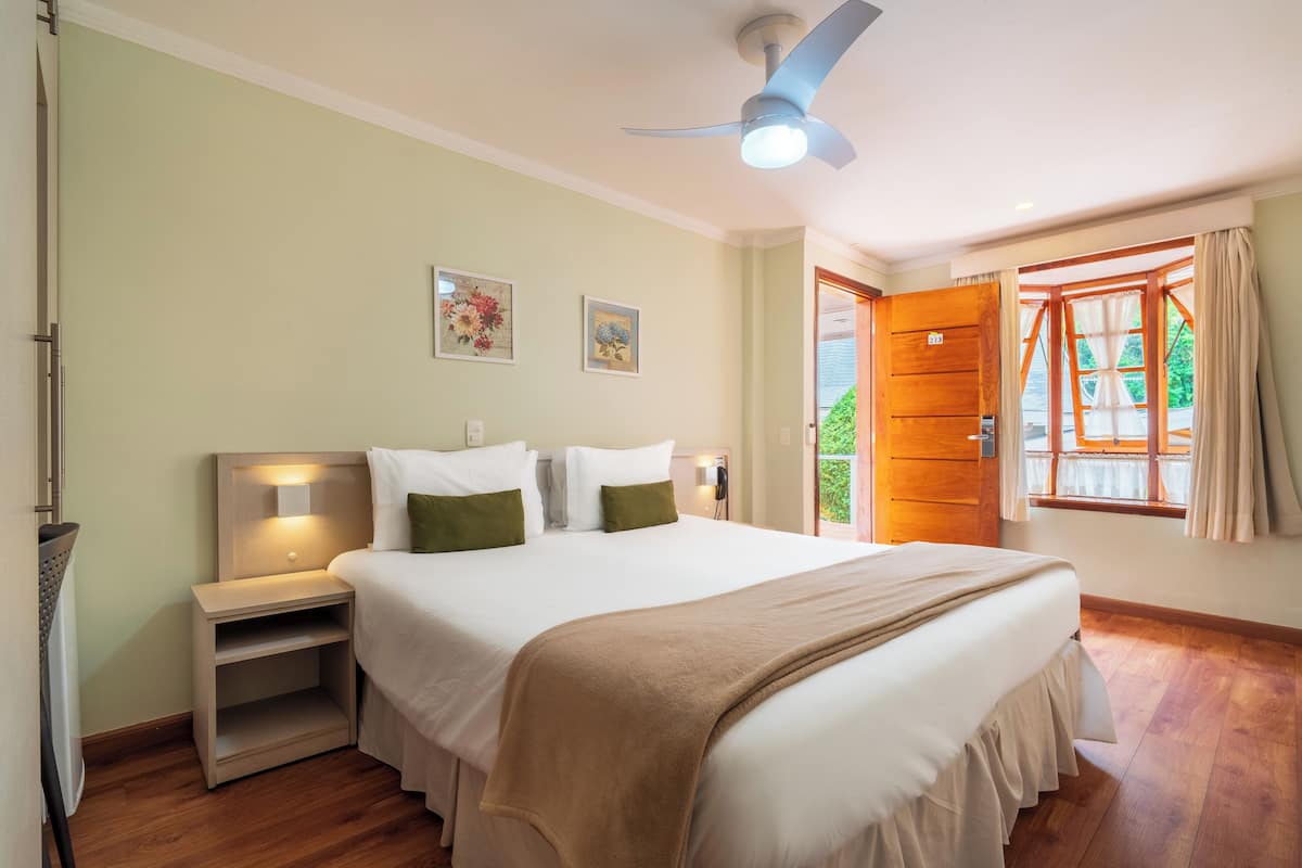 Una cama bien hecha con cabecera, mesitas de noche y un ventilador de techo.