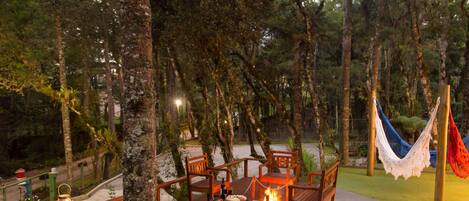 Un espacio al aire libre con una chimenea, sillas de madera y una hamaca.