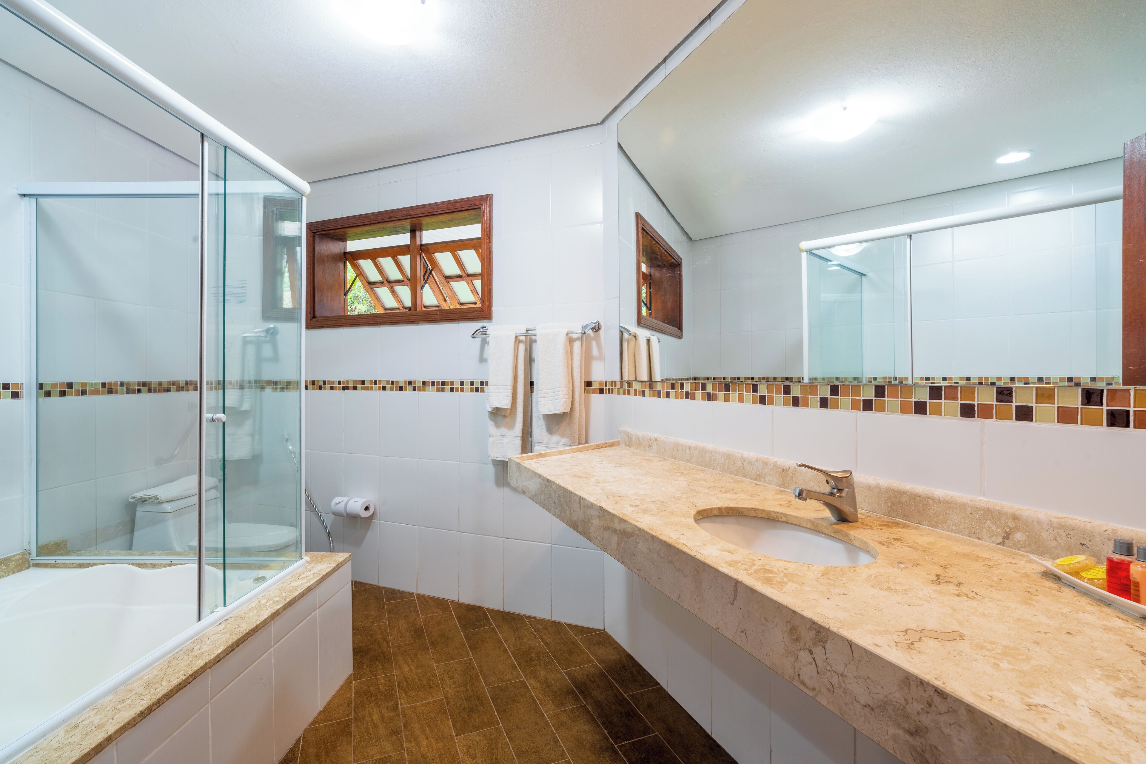 A modern bathroom with a glass-enclosed shower, a sink with a beige countertop, and a large mirror above the sink.