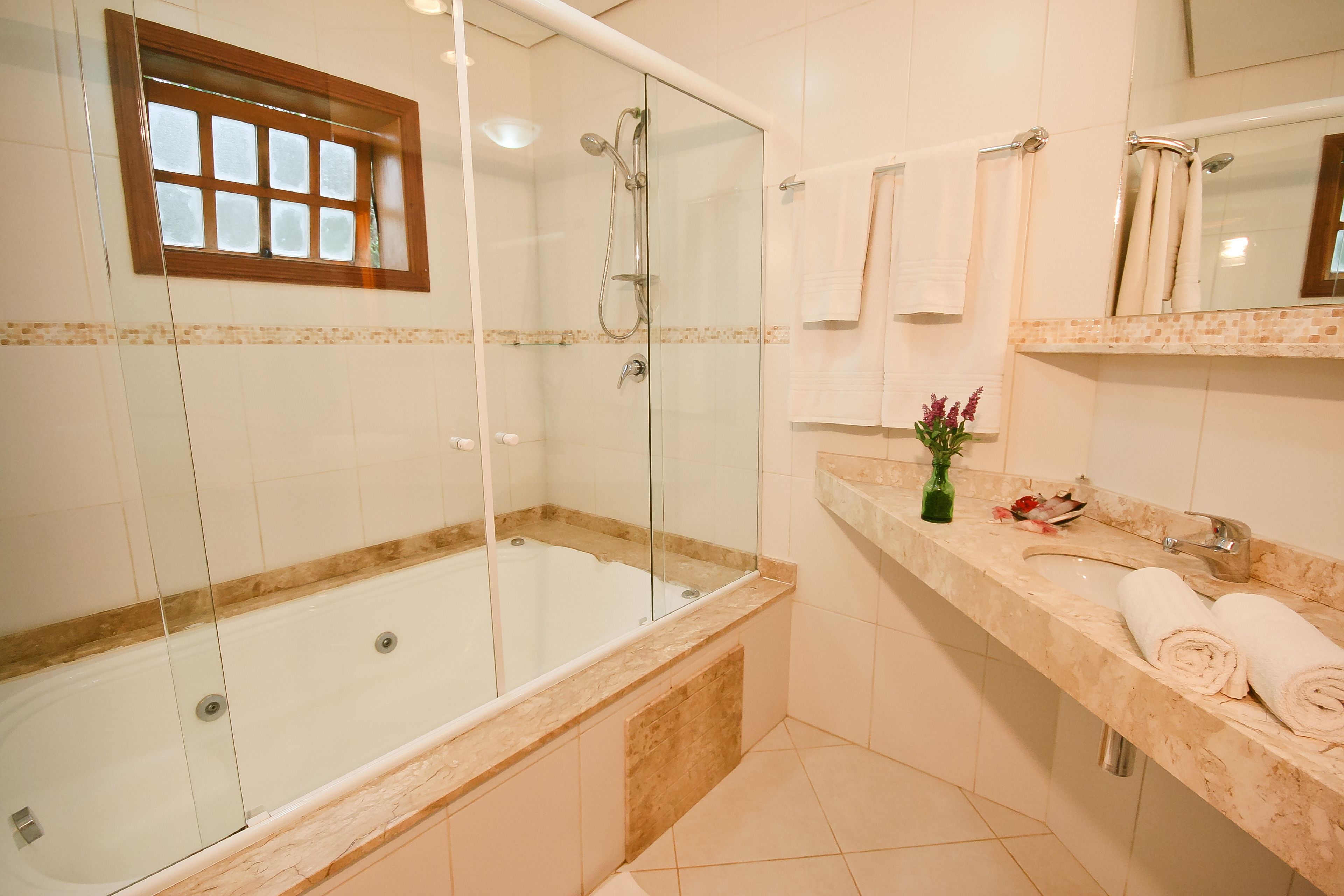 A modern bathroom with a glass-enclosed shower, a bathtub, and a marble countertop with a sink and towel rack.