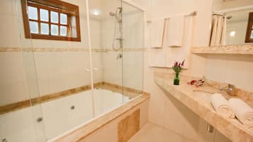 A modern bathroom with a glass-enclosed shower, a bathtub, and a marble countertop with a sink and towel rack.