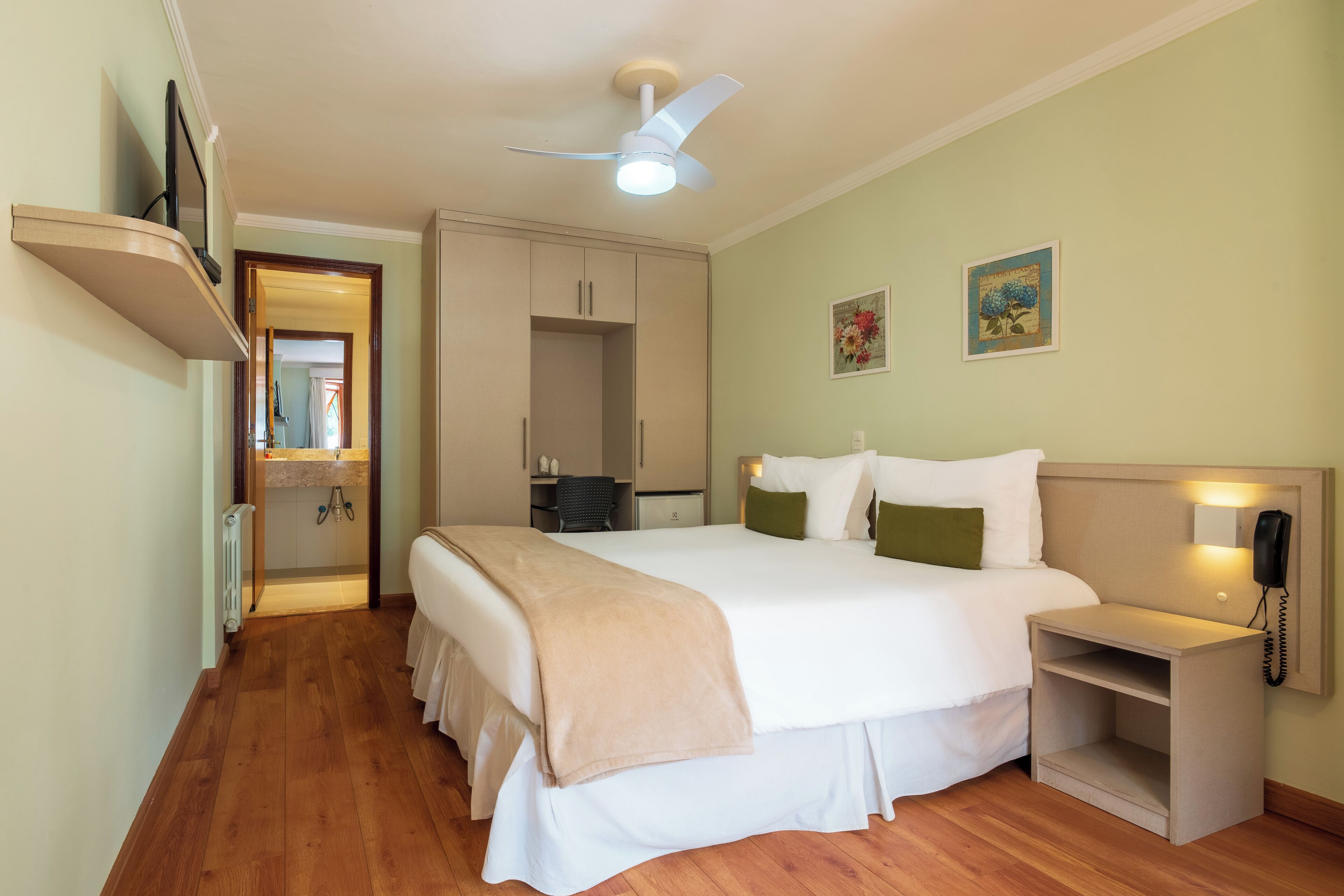 A hotel room with a bed, bedside table, nightstand, and a ceiling fan.