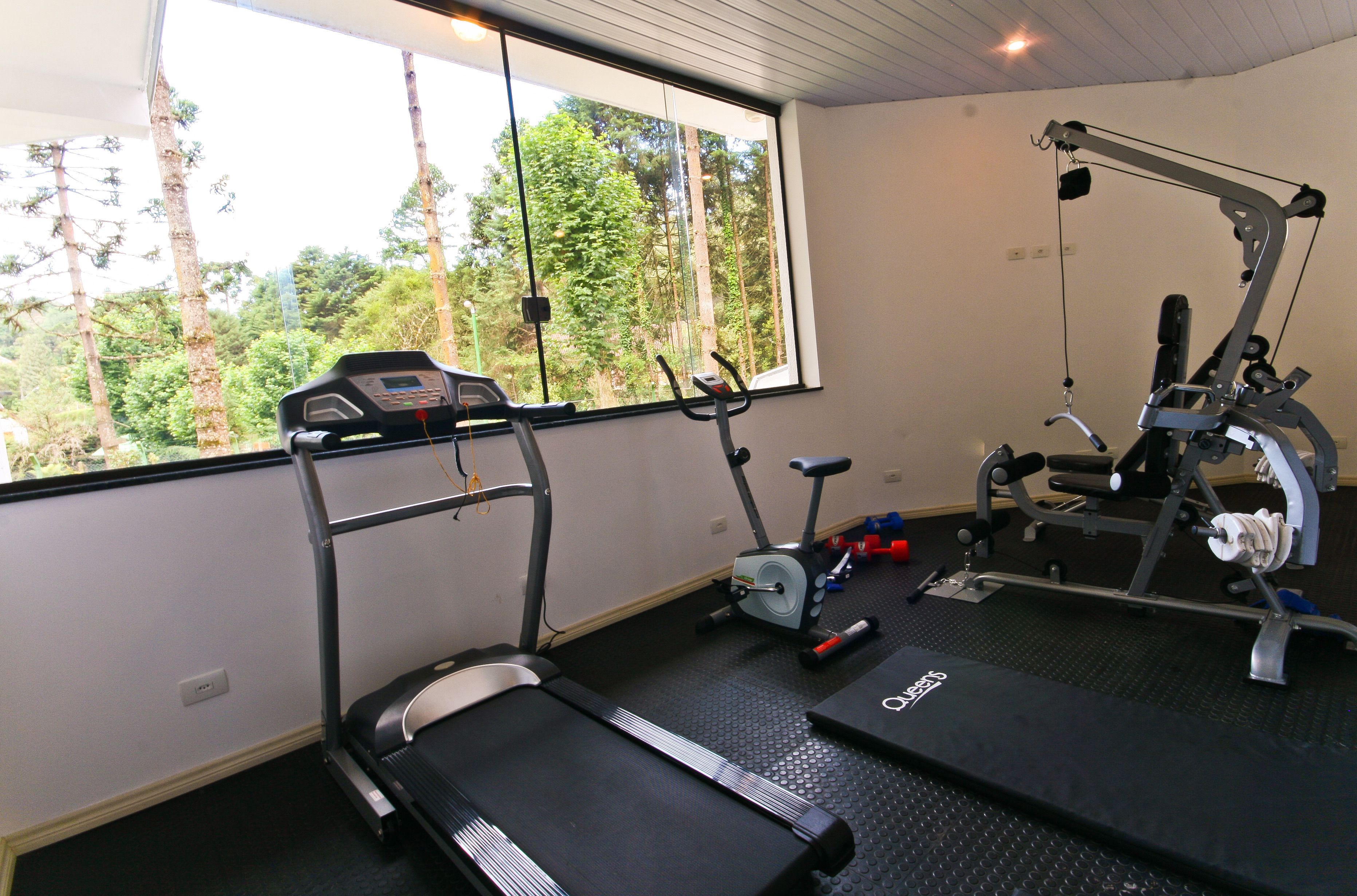 A gym with treadmills, an elliptical, and a weight machine, with a large window overlooking trees.