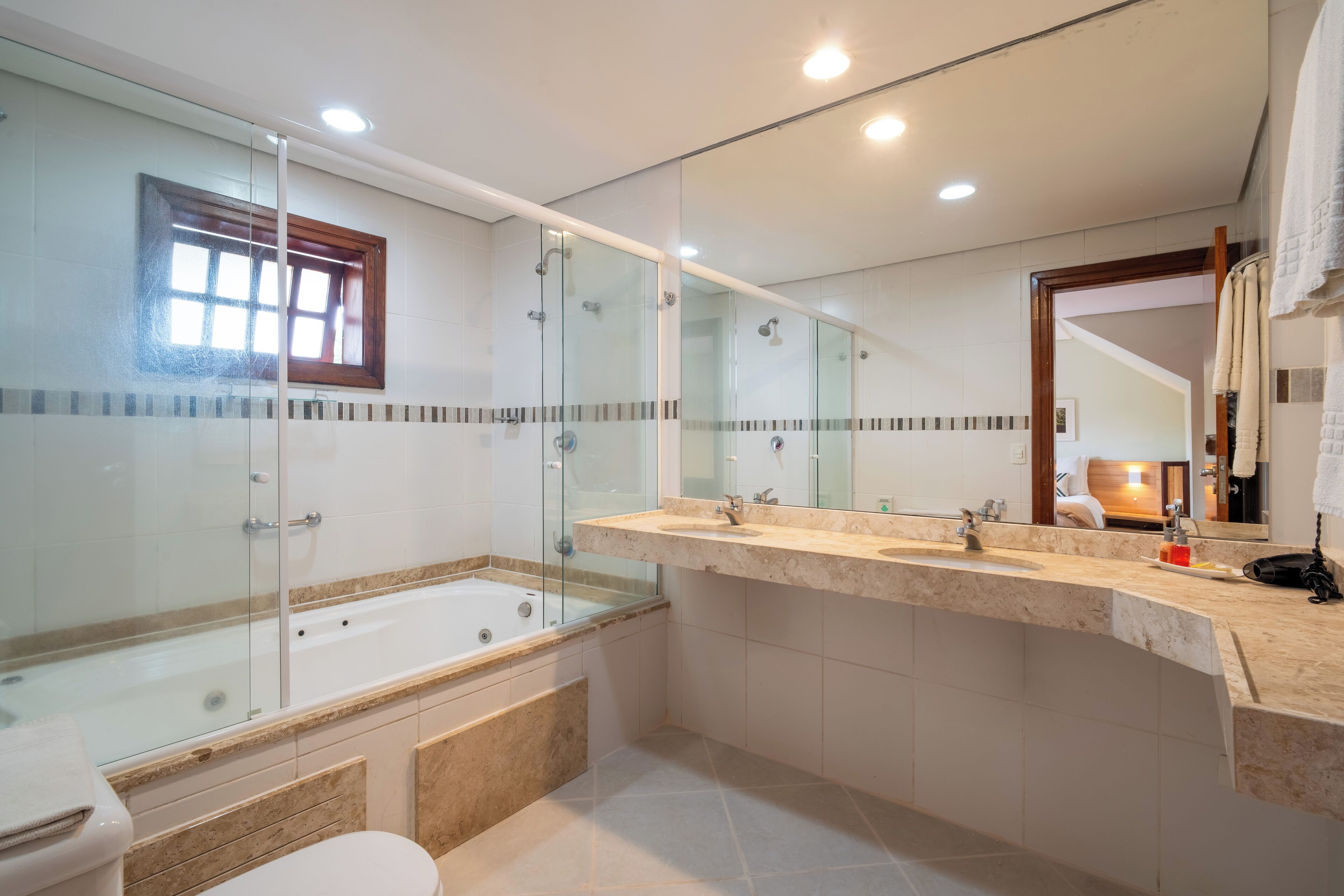 A modern bathroom with a glass-enclosed shower, a bathtub, and a vanity with two sinks.