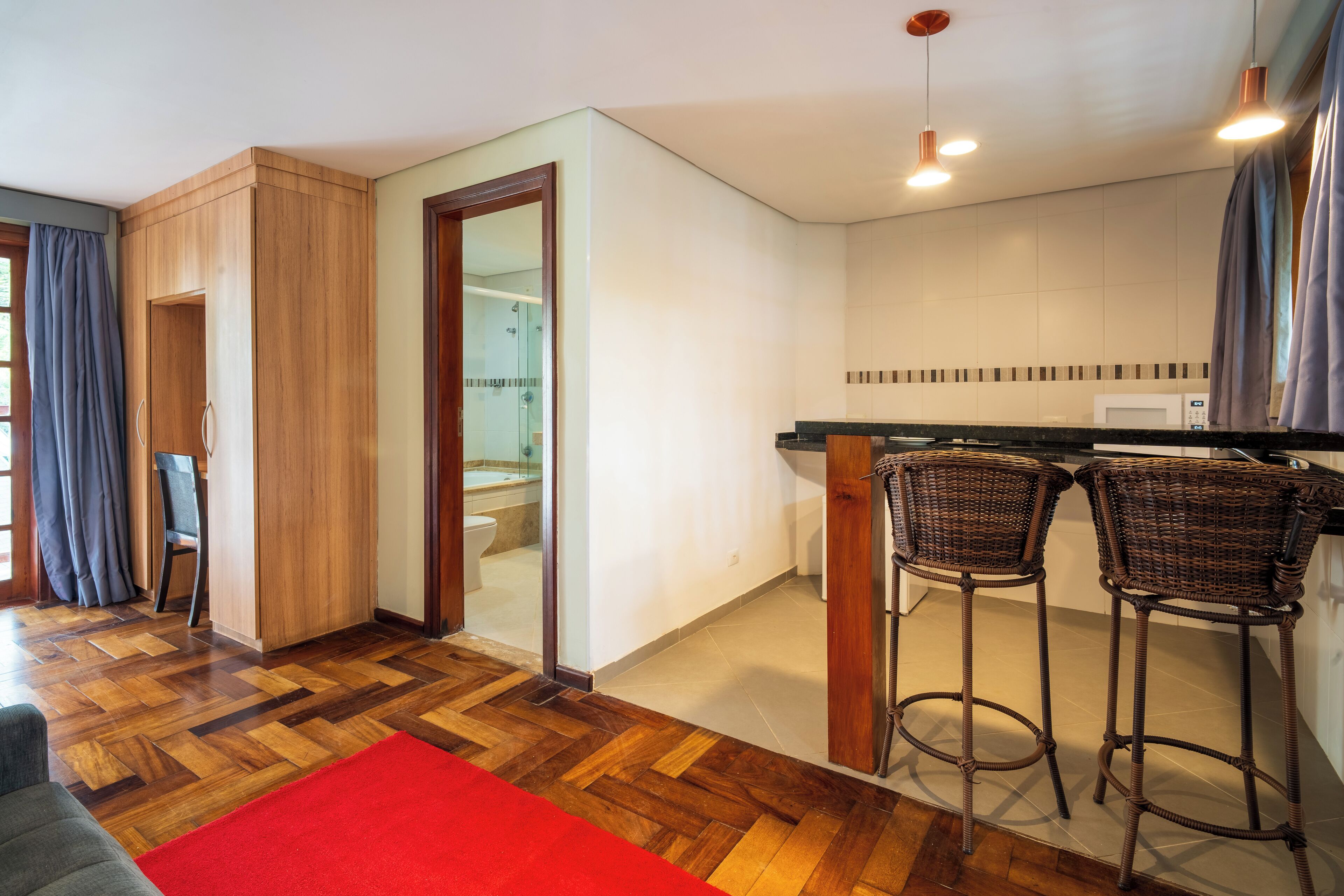 A modern kitchen with wooden flooring, a red rug, and two wicker bar stools.