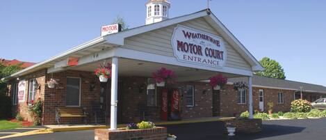 A motor court entrance with a weather vane, a Coca-Cola sign, and flower planters.