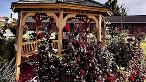A gazebo with a weather vane, surrounded by various plants and flowers. - Weathervane Motor Court (Ronks)