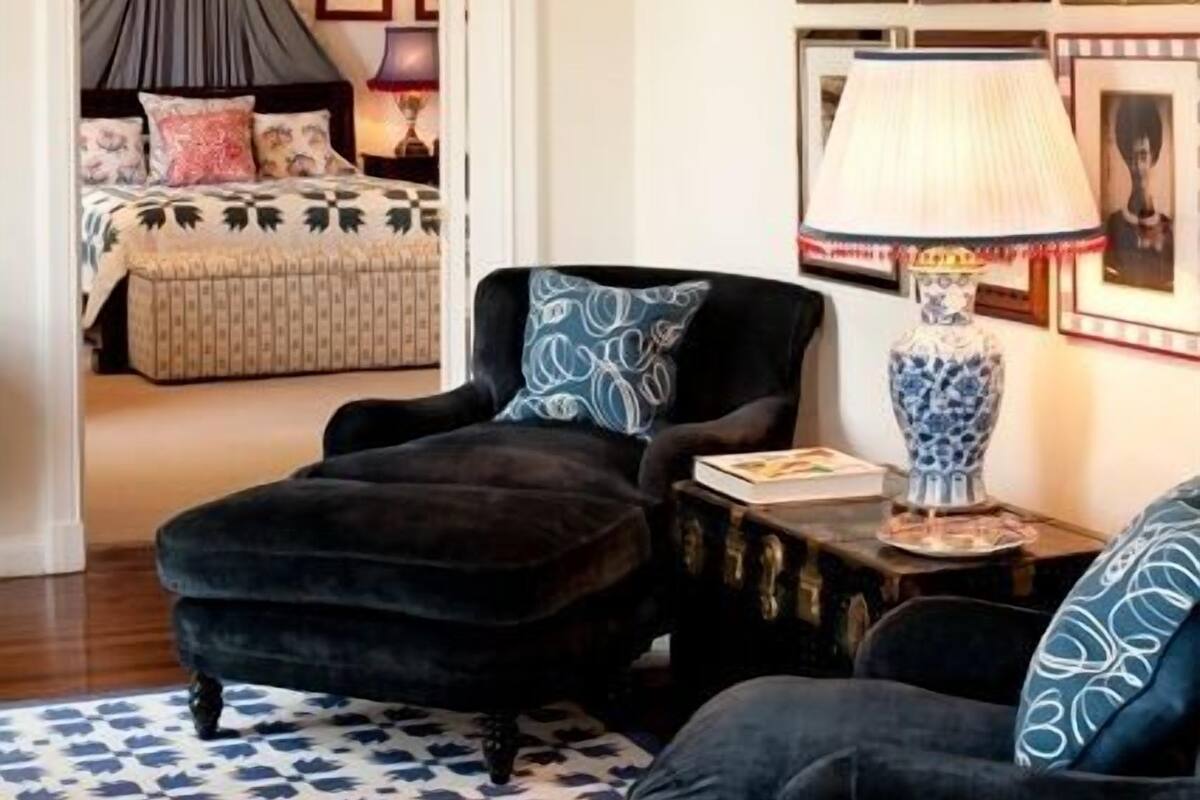 A room with a chandelier, a bed with a canopy, a patterned rug, and framed pictures on the wall.