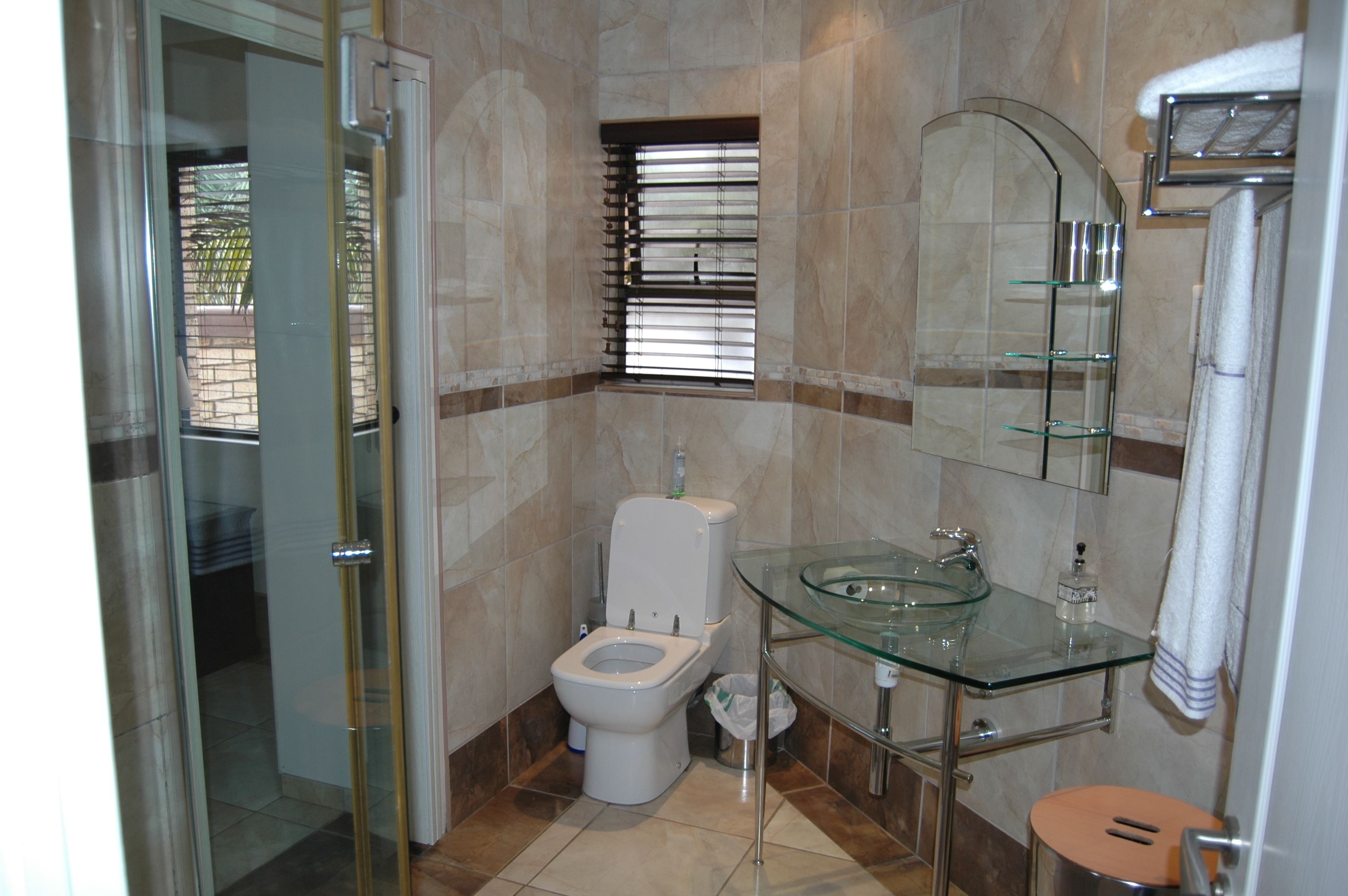 A bathroom with a glass sink, a toilet, and a shower area.