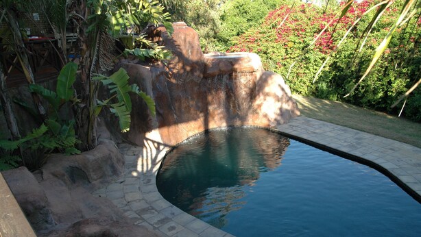 A swimming pool with a natural rock design, surrounded by lush greenery and a stone pathway. - Bon a Vie B and B and Self Catering (East London)