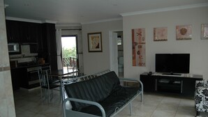 A living room with a black leather sofa, a TV, and a dining area with chairs and a table. - Bon a Vie B and B and Self Catering (East London)