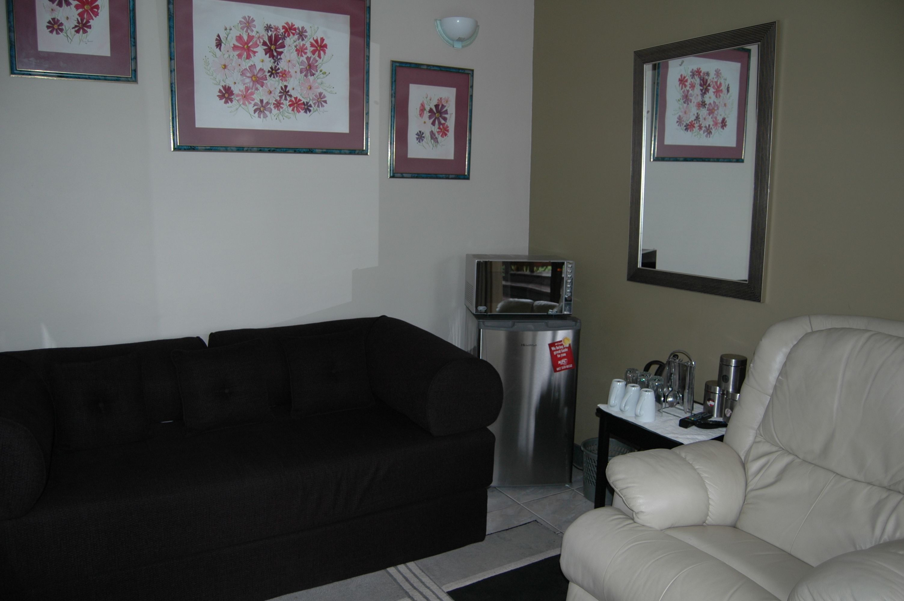 Un salon avec un canapé noir, un fauteuil en cuir blanc et une petite table sur laquelle se trouvent une poubelle et un four à micro-ondes.