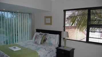 A bedroom with a bed, a nightstand, a window with blinds, and a framed picture on the wall.
