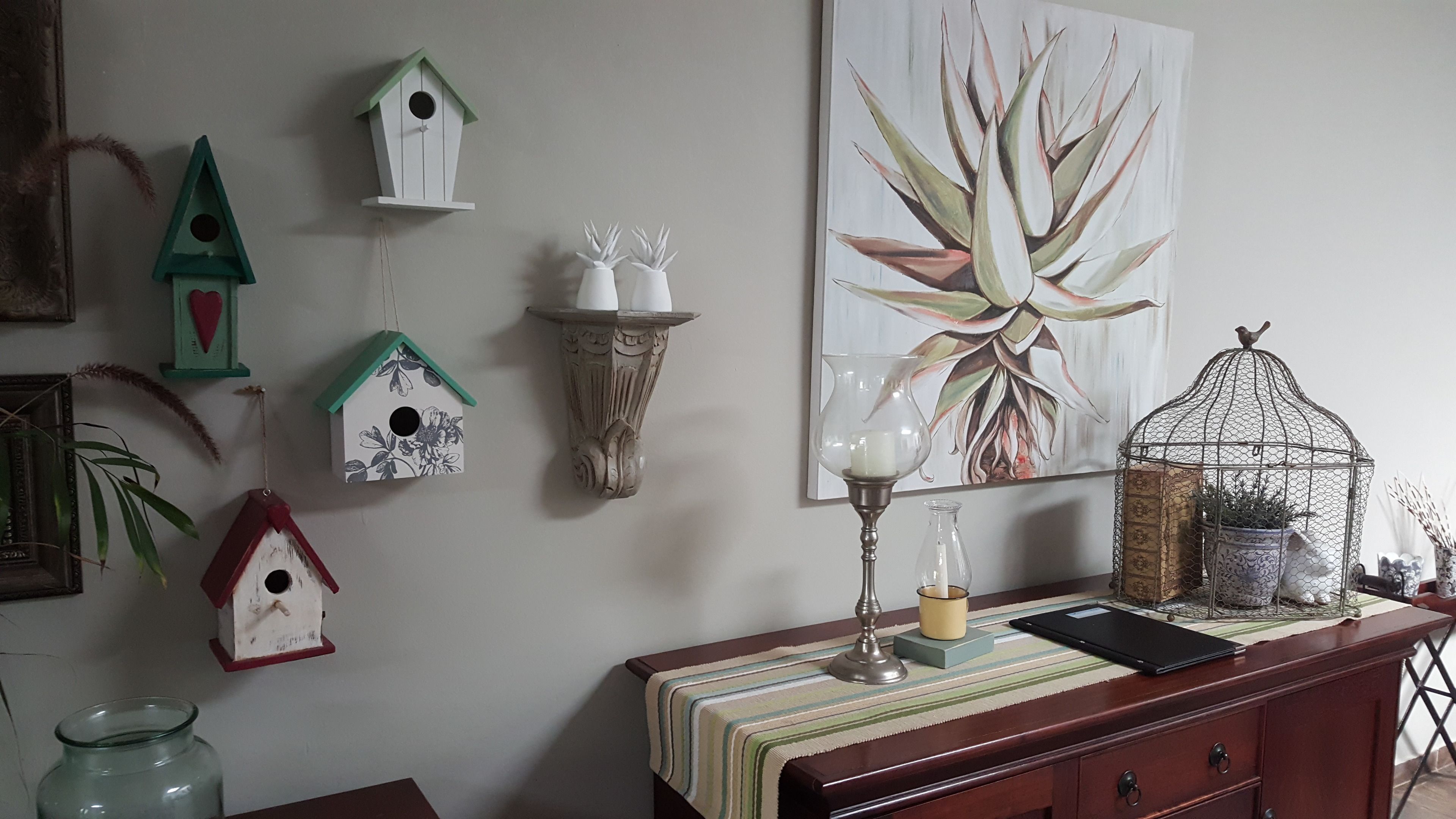 A wall with various birdhouses and a large plant painting.