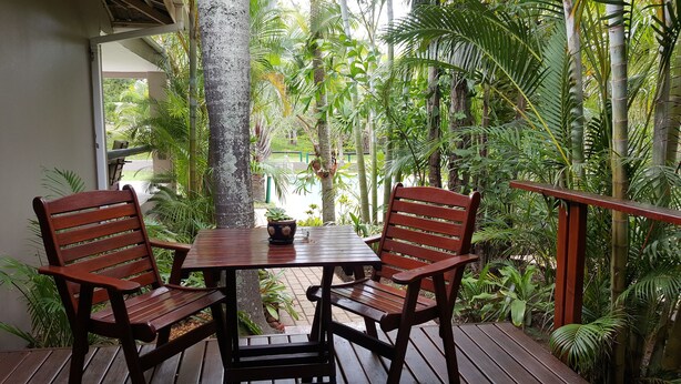 A wooden table and chairs on a deck with a view of tropical plants and a building in the background. - Sandpiper Guest House (St. Lucia)