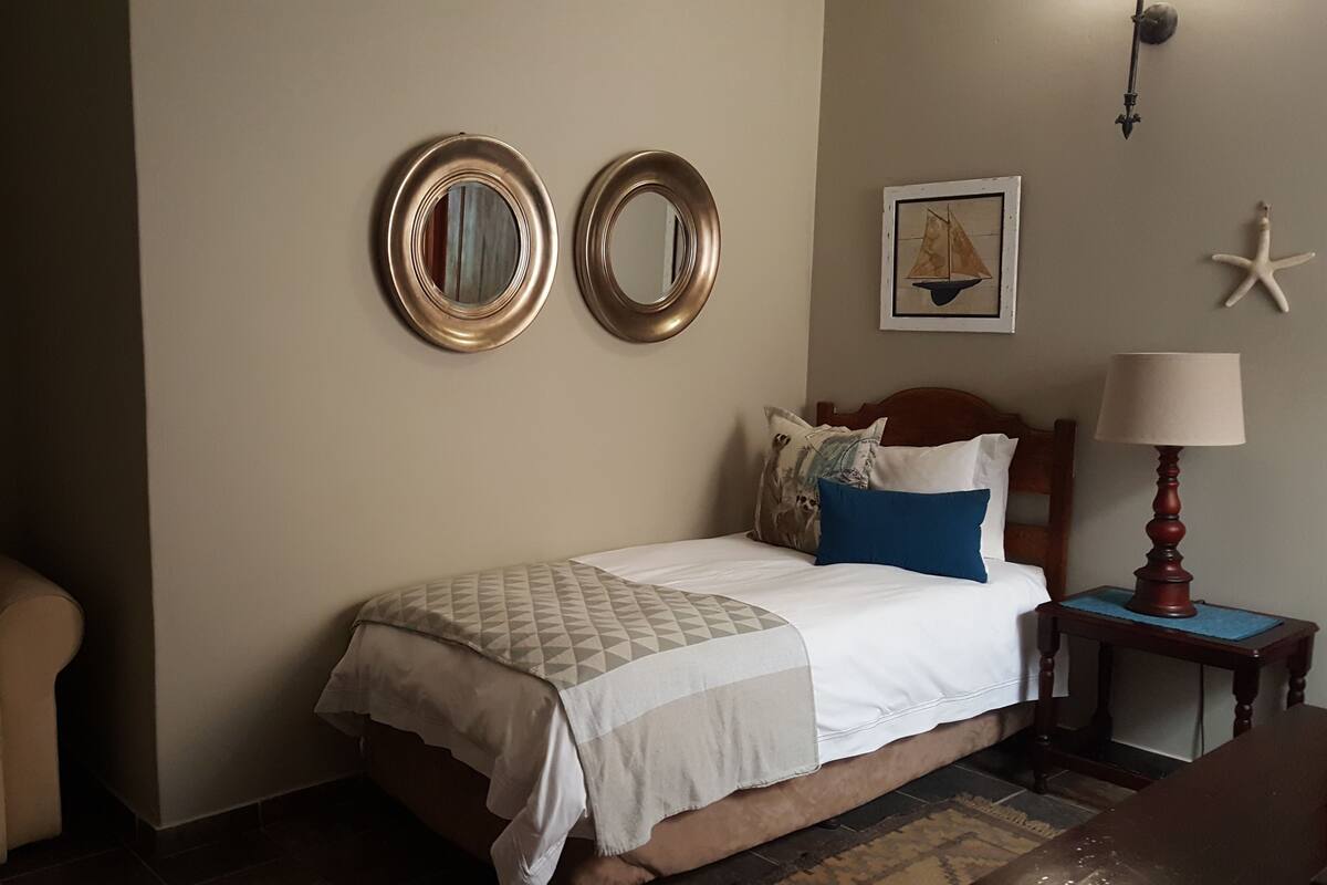 A hotel room with a bed, a nightstand, a lamp, a chair, and wall decorations including two mirrors and a framed picture.