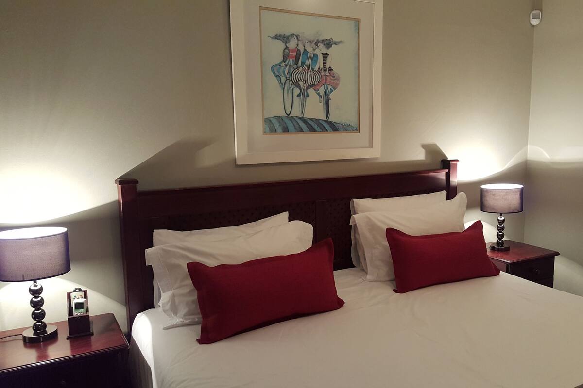 A hotel room with a bed, two nightstands, a lamp, a mirror, and a painting on the wall.