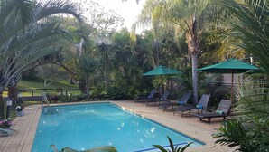A swimming pool with lounge chairs and umbrellas, surrounded by lush greenery. - Sandpiper Guest House (St. Lucia)