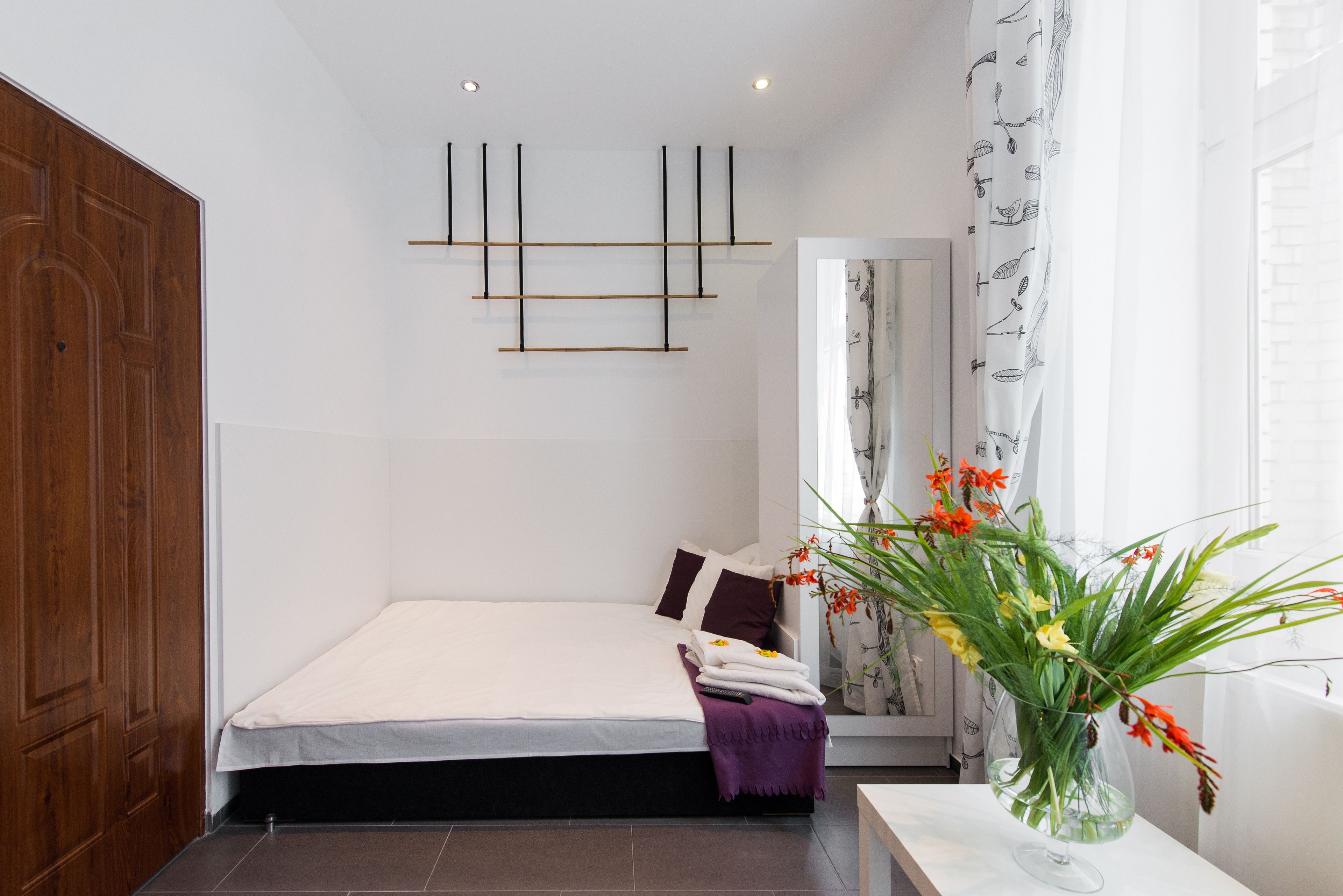 A bedroom with a bed, a wooden wardrobe, a wall-mounted light fixture, and a window with curtains.