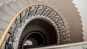 Un escalier en colimaçon avec des rampes en métal ouvragé et des marches en pierre.