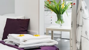 Un lit bien fait, avec un oreiller violet, une pile de serviettes blanches et une télécommande.
