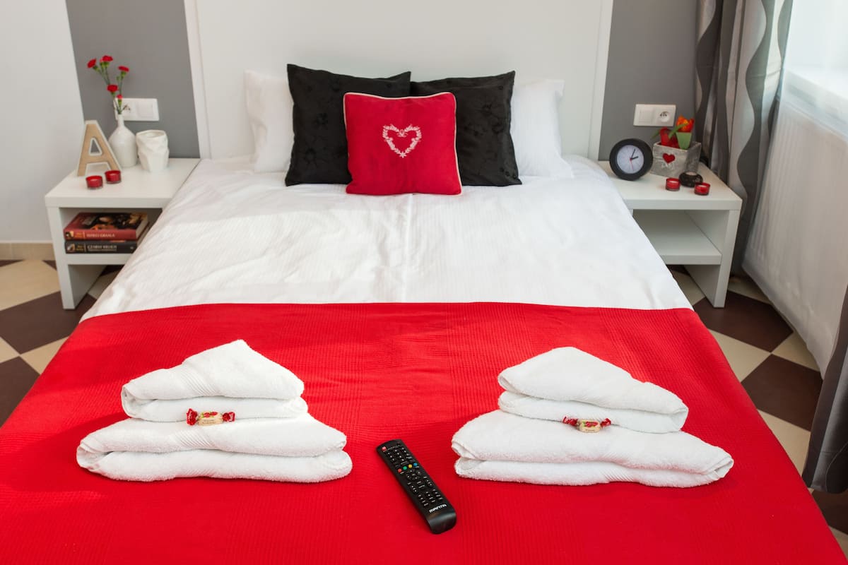 A hotel room with a neatly made bed, a red blanket, and a remote control on the bed.