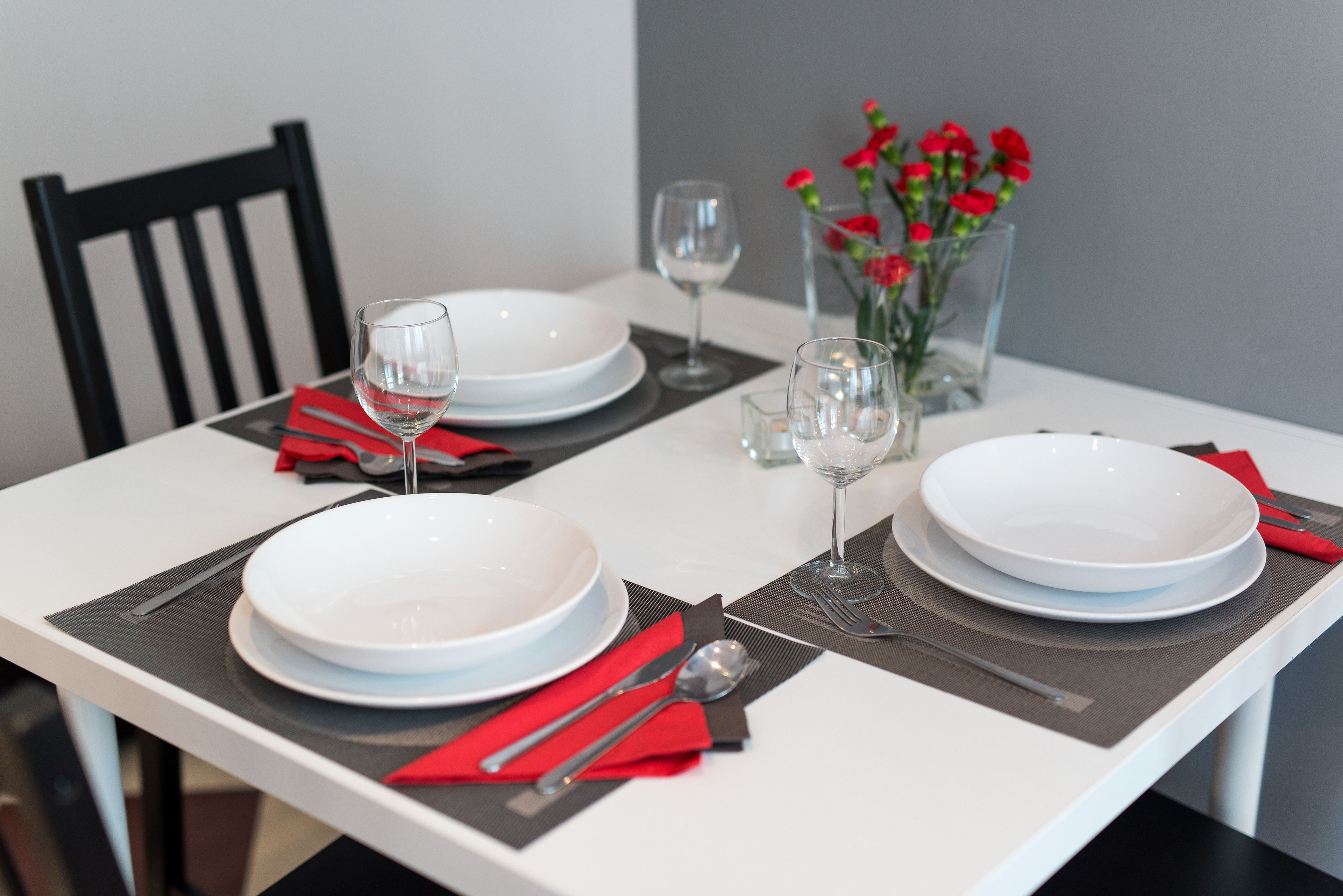Een eettafel gedekt met witte borden, rode servetten en heldere glazen.