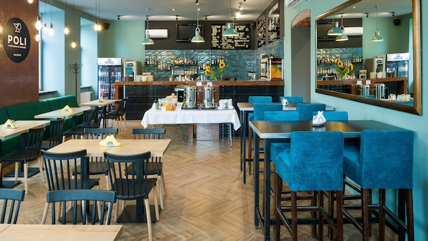 L’intérieur d’un restaurant est aménagé avec des tables et des chaises en bois, un coin bar et un grand miroir sur le mur.