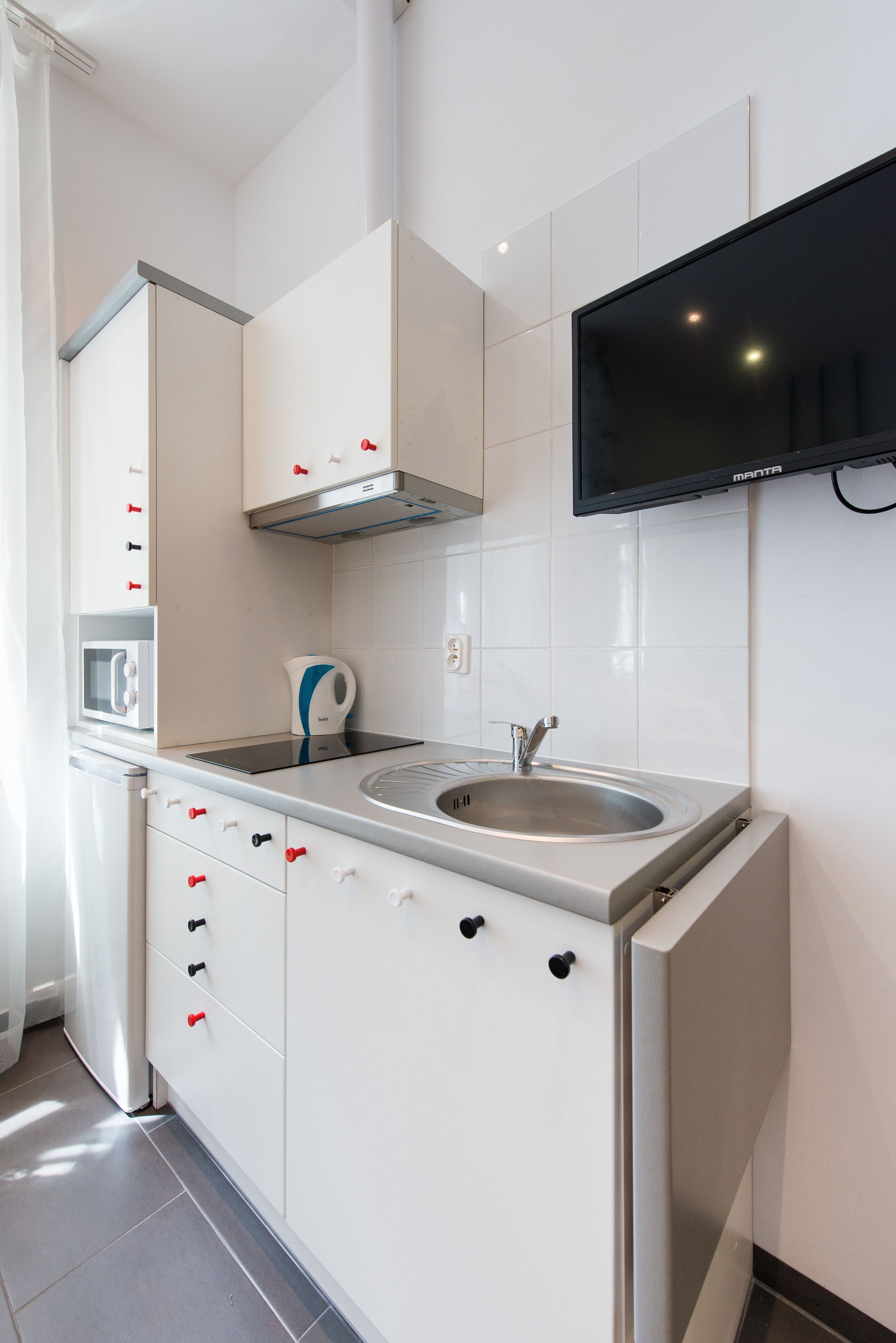 A modern kitchen with white cabinets, a stainless steel sink, a microwave, and a flat-screen TV mounted on the wall.
