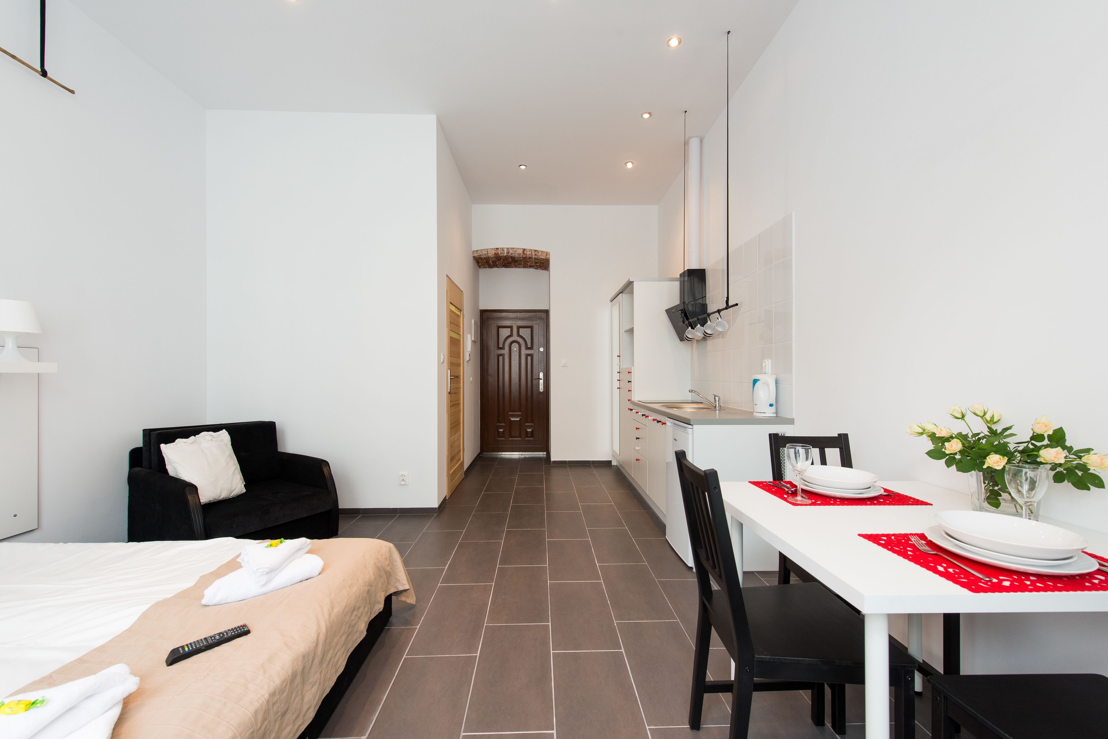 A hotel room with a bed, a sitting area with a black sofa, a dining table set with plates and a vase of flowers.