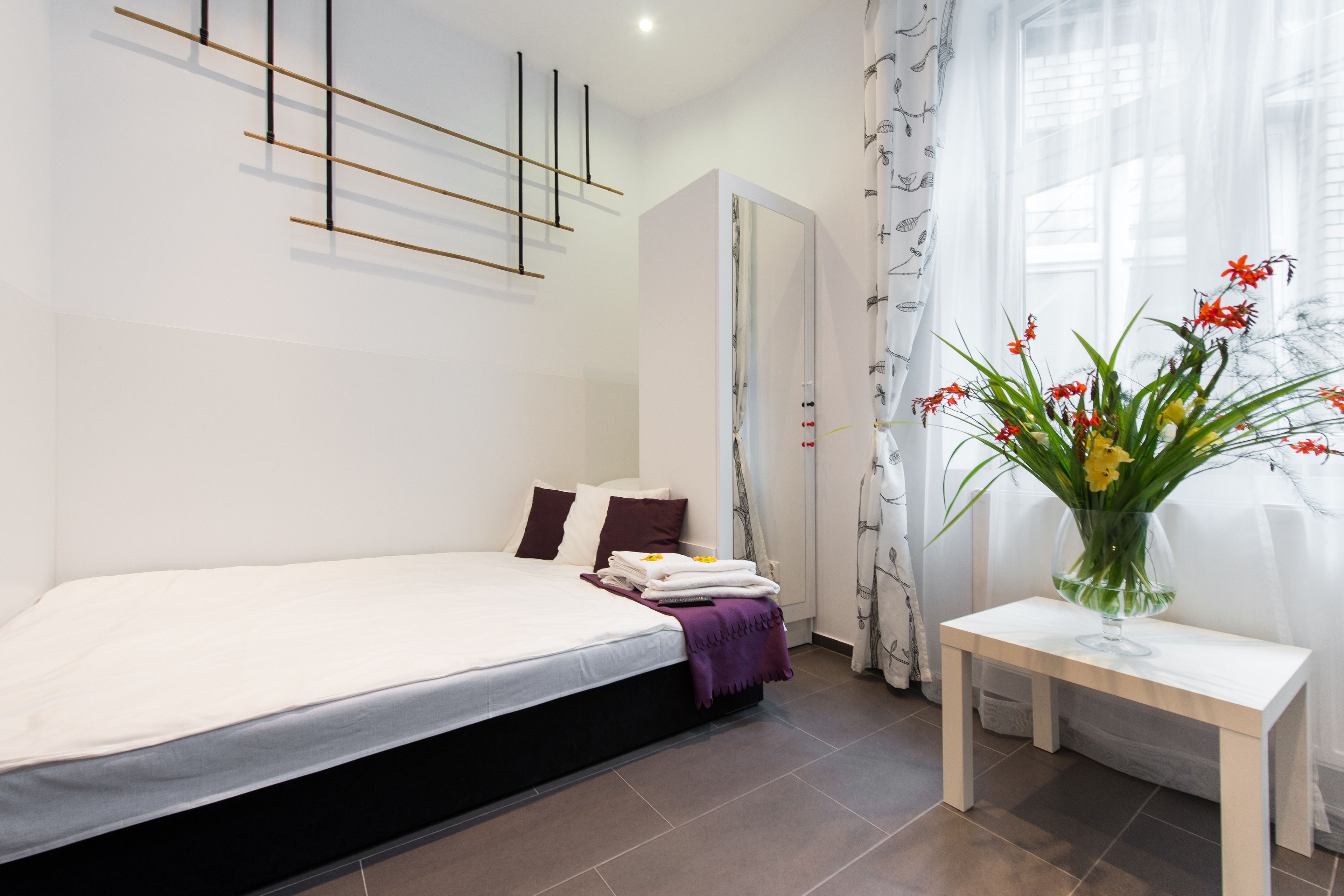 A modern bedroom with a bed, a bedside table, a mirror, and a window with curtains.